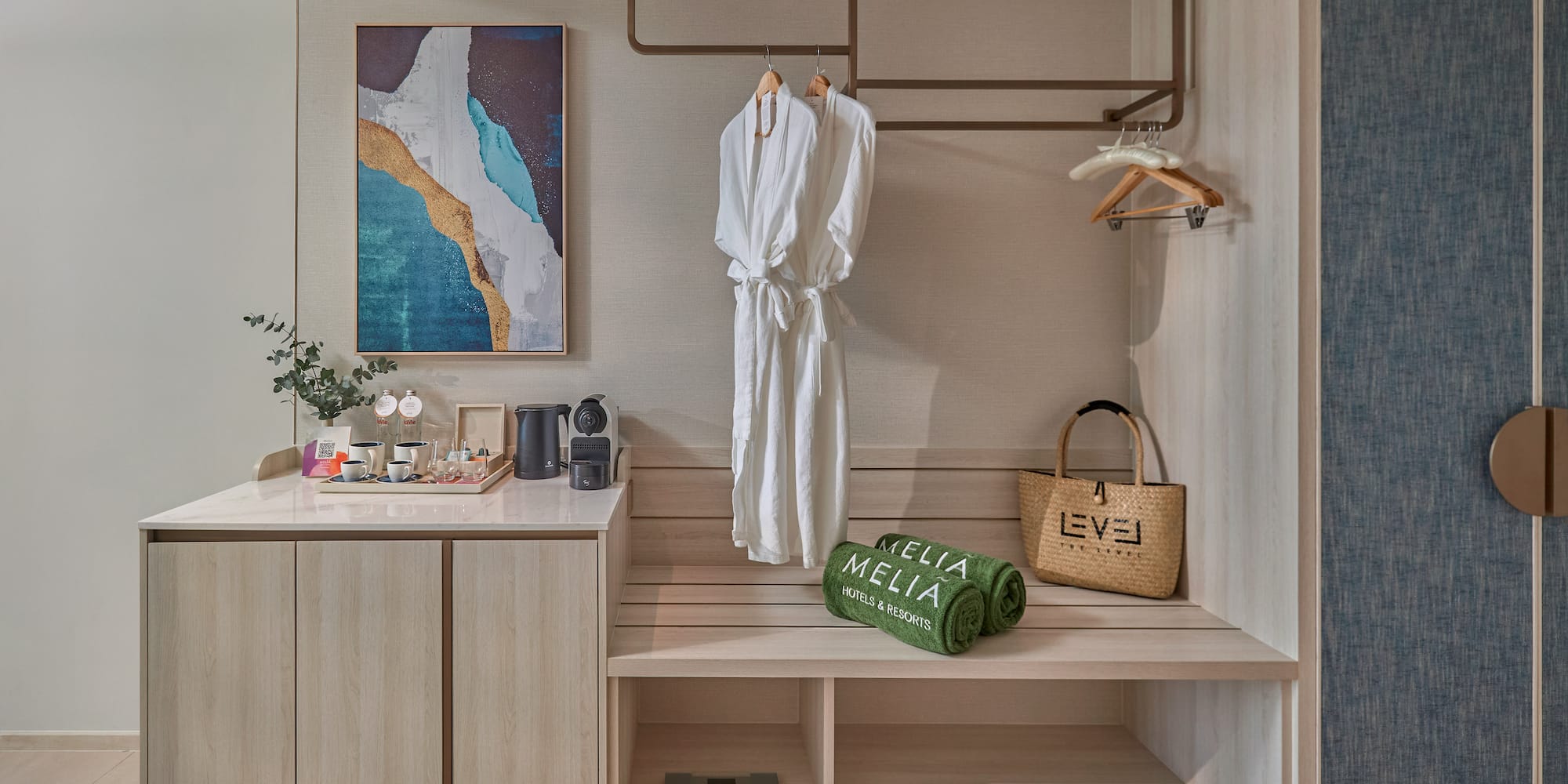 Hotel room wardrobe with bathrobes, Meliá towels, coffee station, and abstract art.