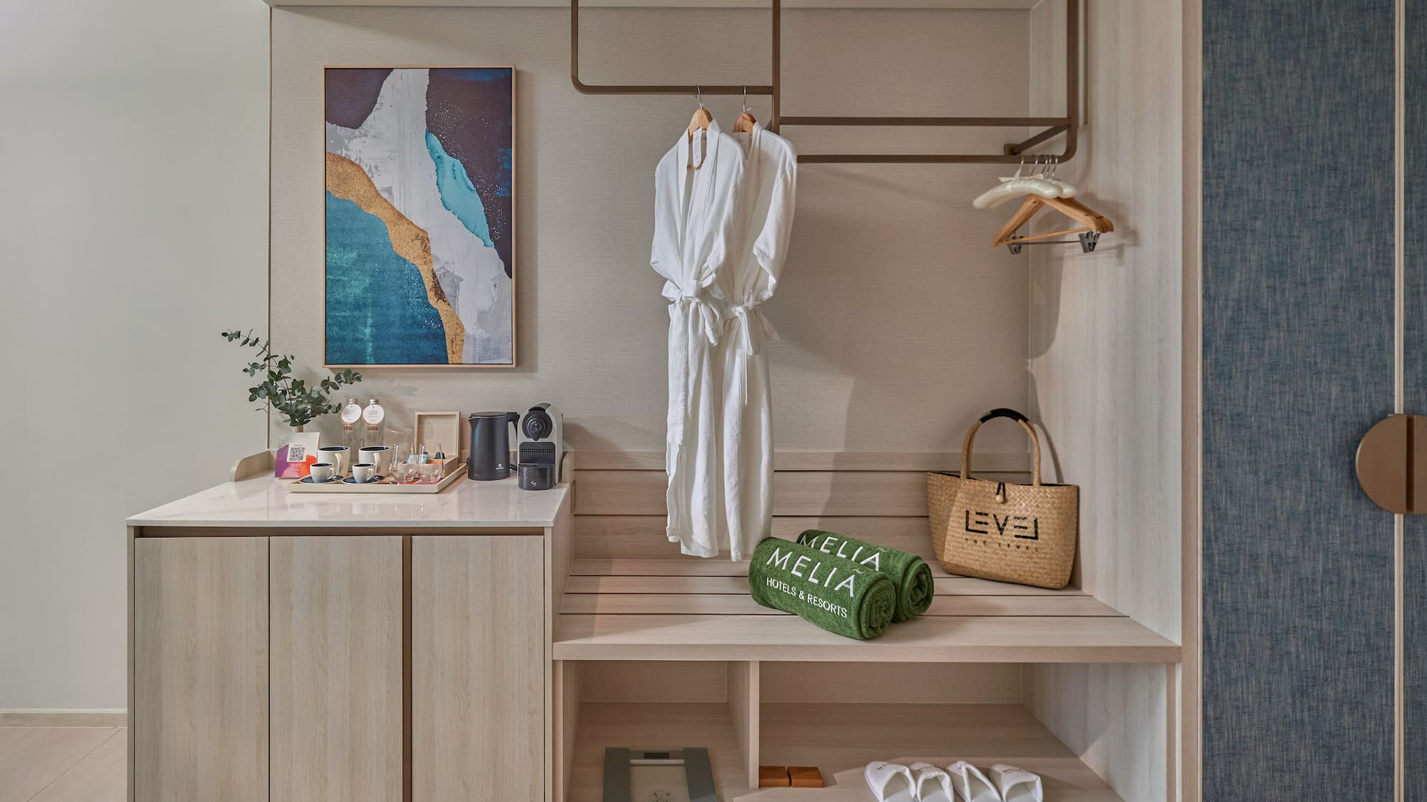 Hotel room wardrobe with bathrobes, Meliá towels, coffee station, and abstract art.