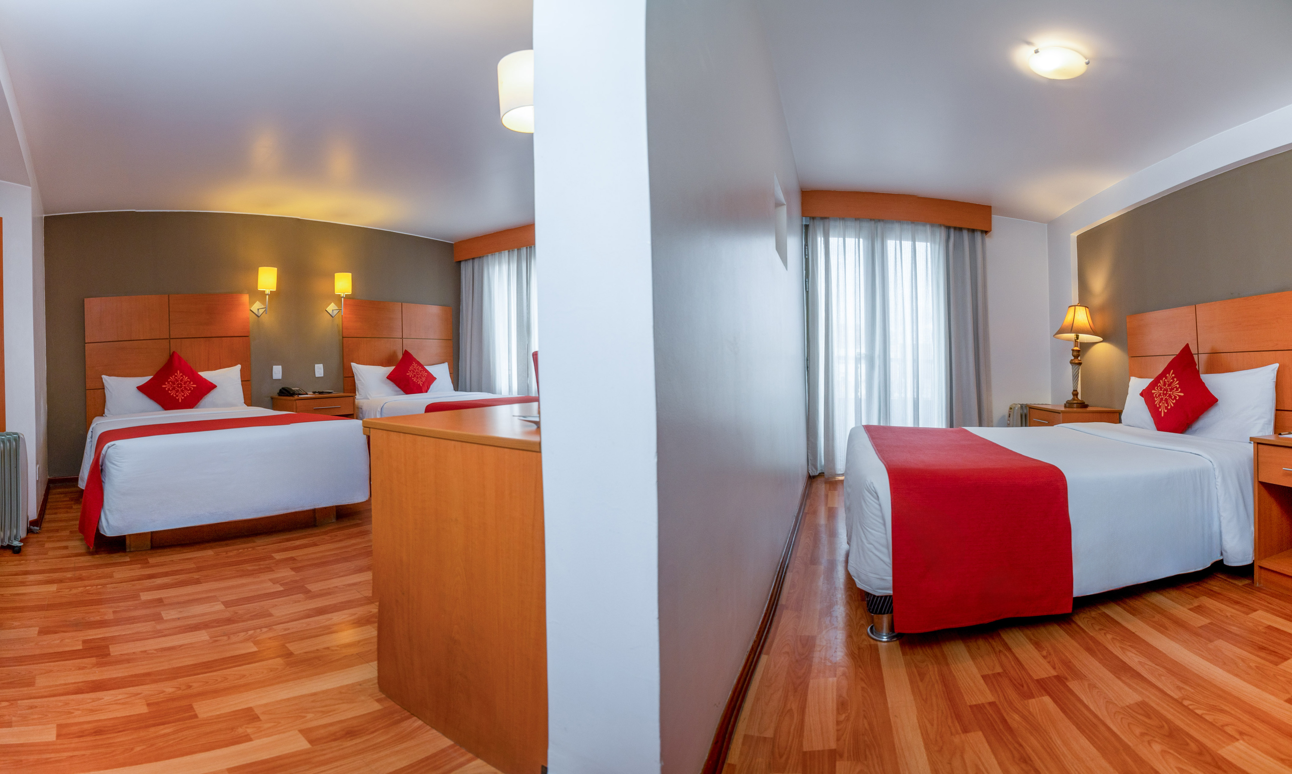 Spacious hotel room featuring three beds, red bedding, and wooden floors.