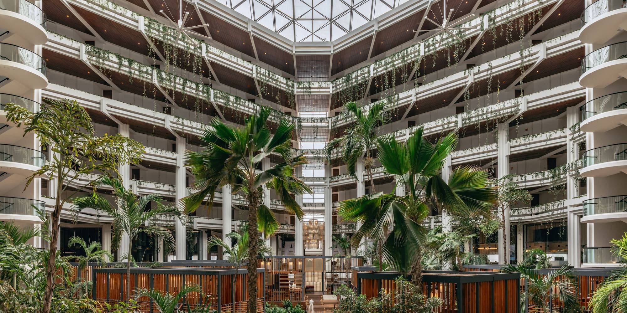 Spacious hotel atrium with glass roof, tropical plants, and modern balconies.