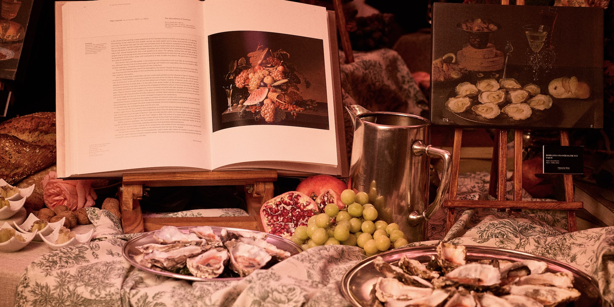 Opulent display: fresh oysters, fruit, open art books with still life art.