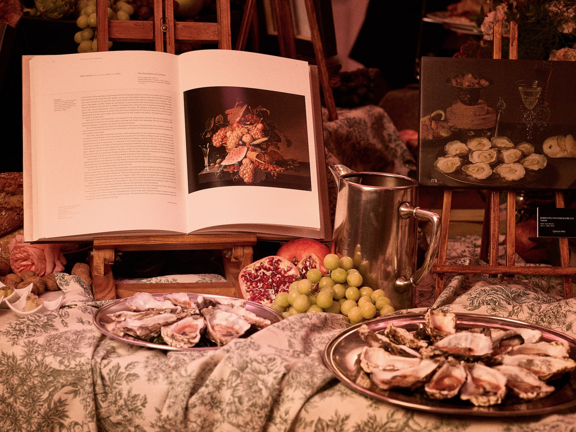 Oysters, grapes, pomegranates, and art books showing still life paintings.