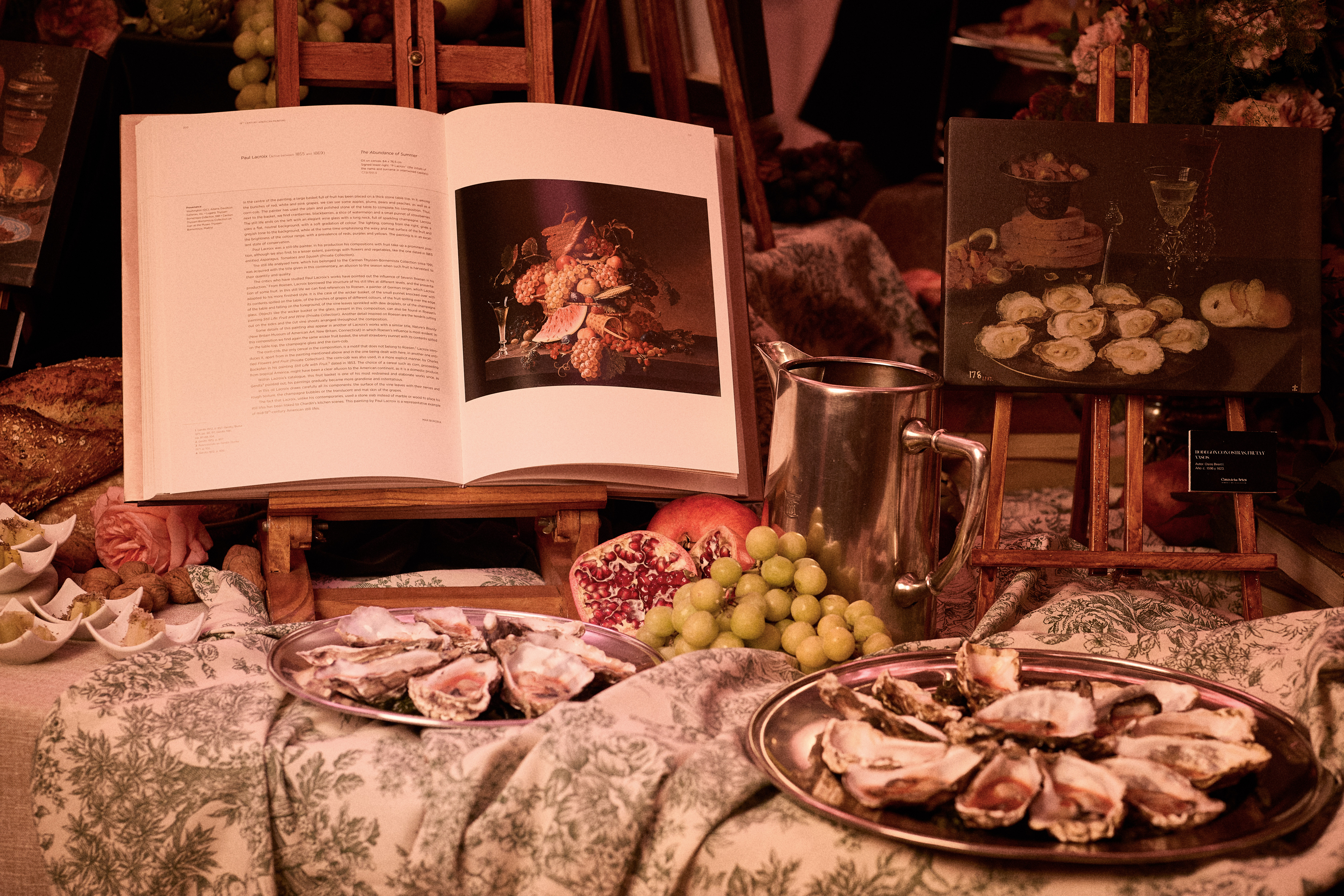 Opulent display: fresh oysters, fruit, open art books with still life art.