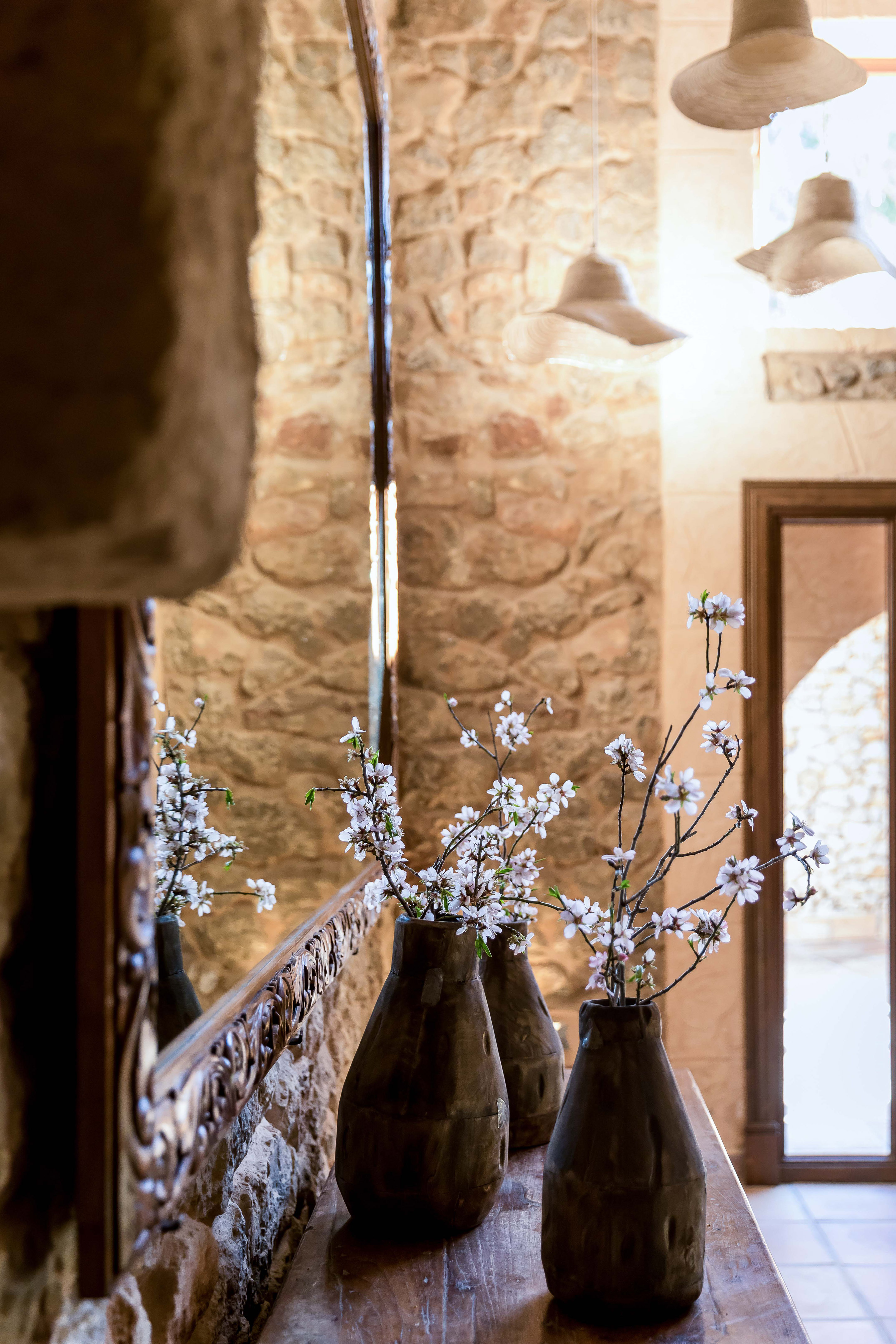 Rustic interior with blooming branches in dark vases, mirror reflection, stone wall.