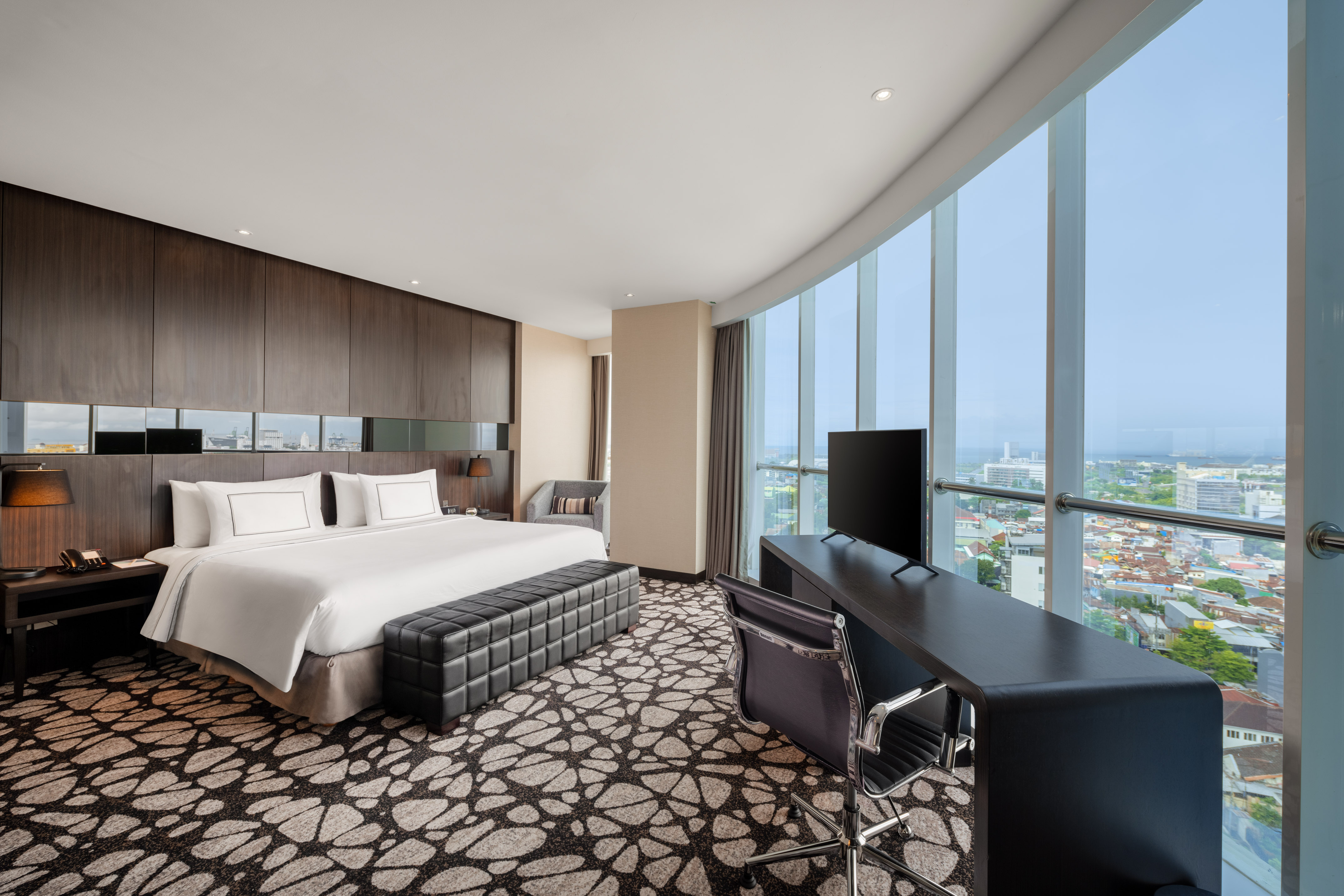 Modern hotel bedroom with king bed, desk, TV, and panoramic city view.