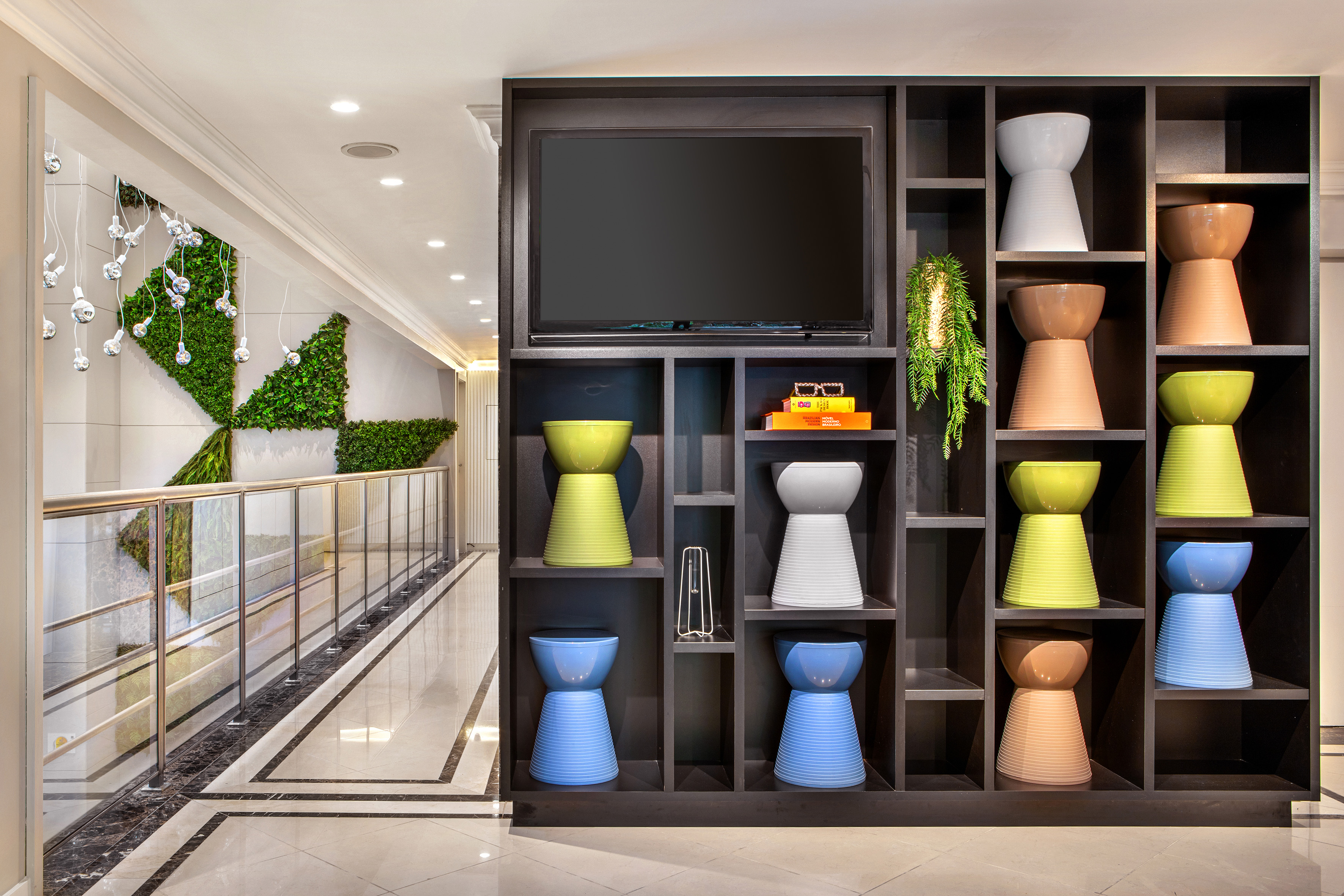 Modern interior: colorful stools on dark shelves, integrated TV, green wall accent.