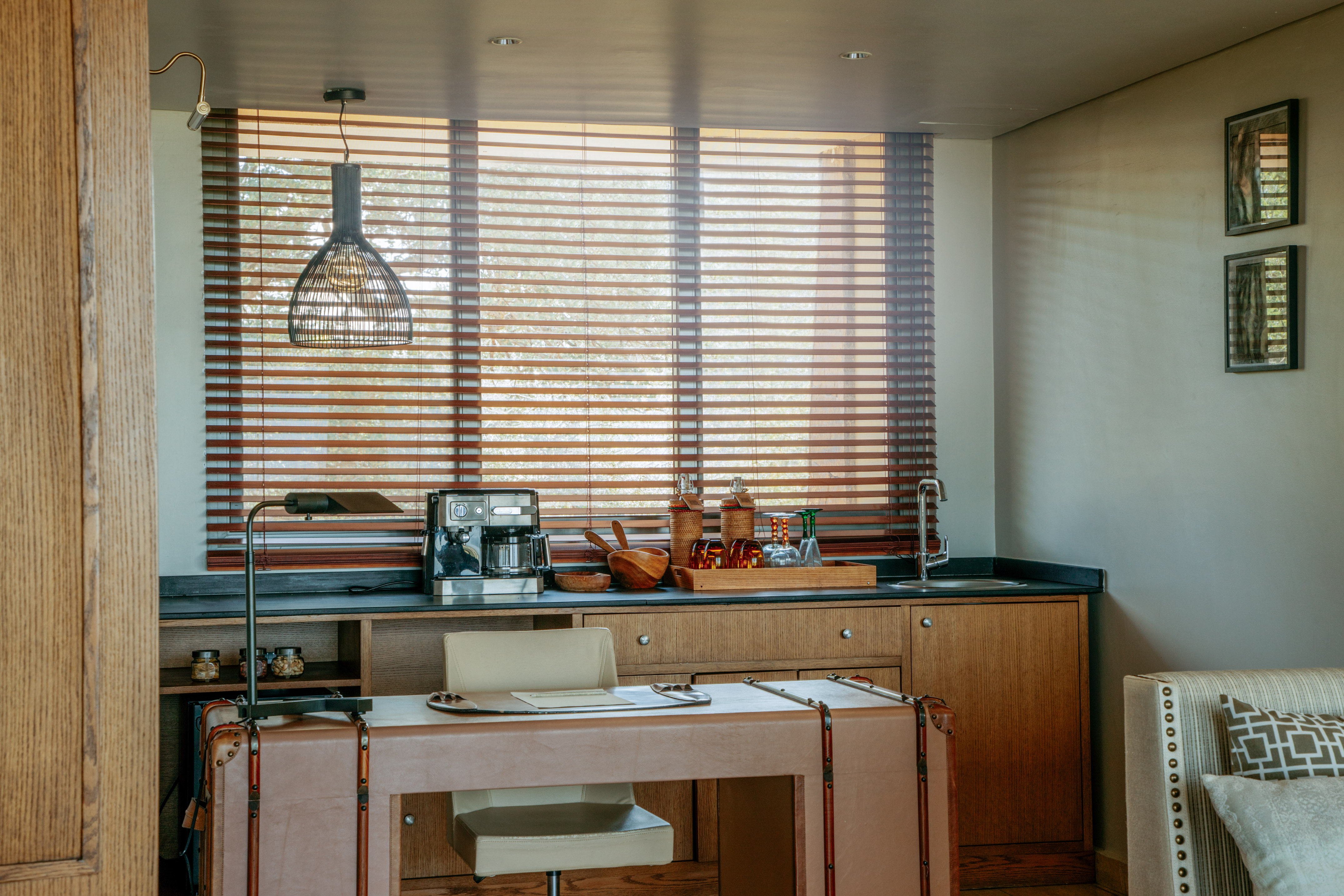 Modern wet bar and coffee station with a desk and wooden blinds.