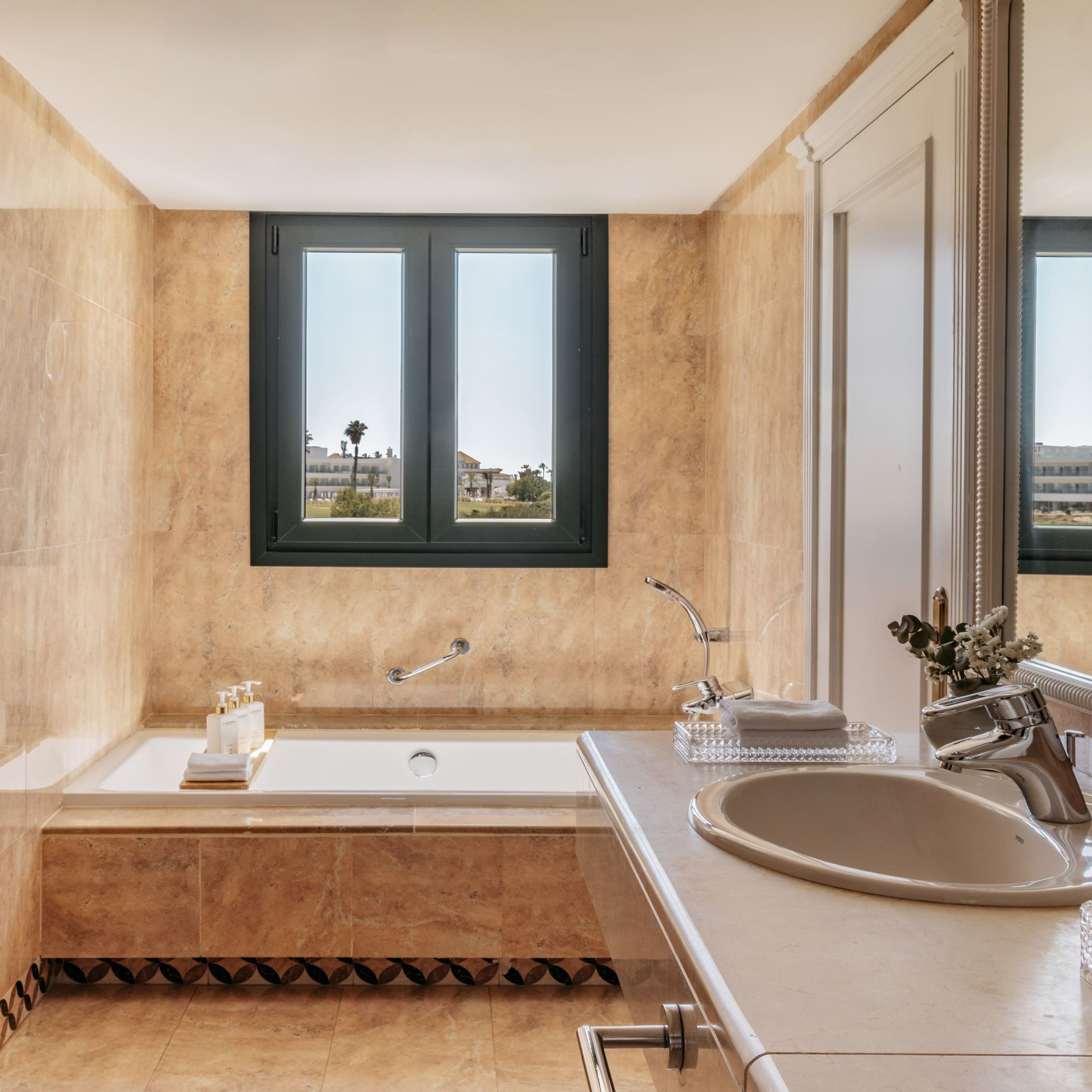 Elegant beige marble bathroom with built-in tub and outdoor window view.