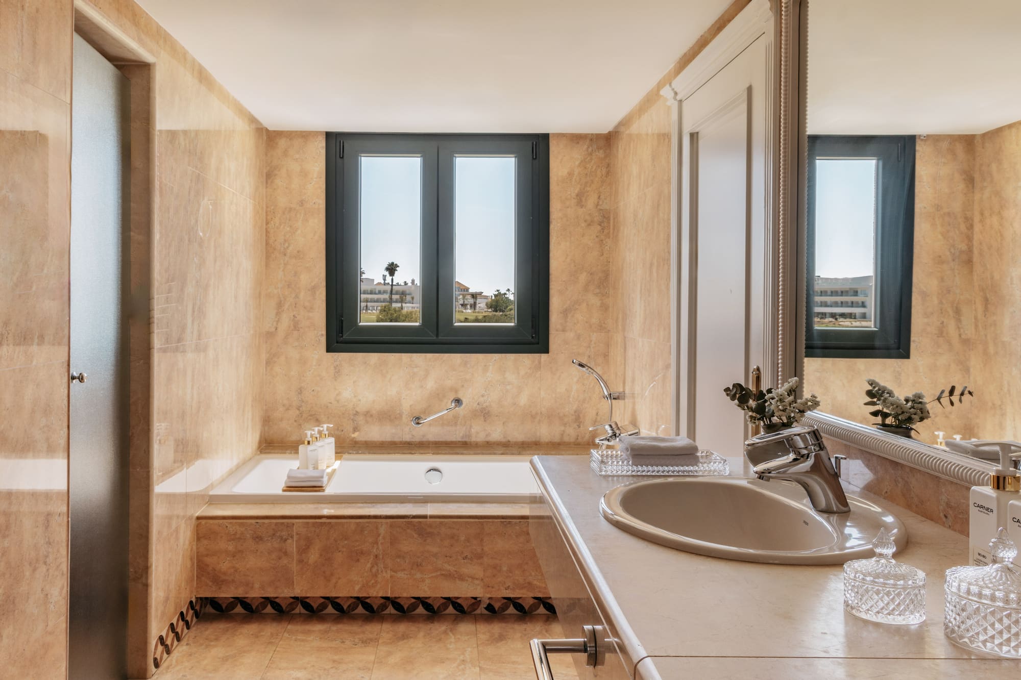 Elegant beige marble bathroom with built-in tub and outdoor window view.
