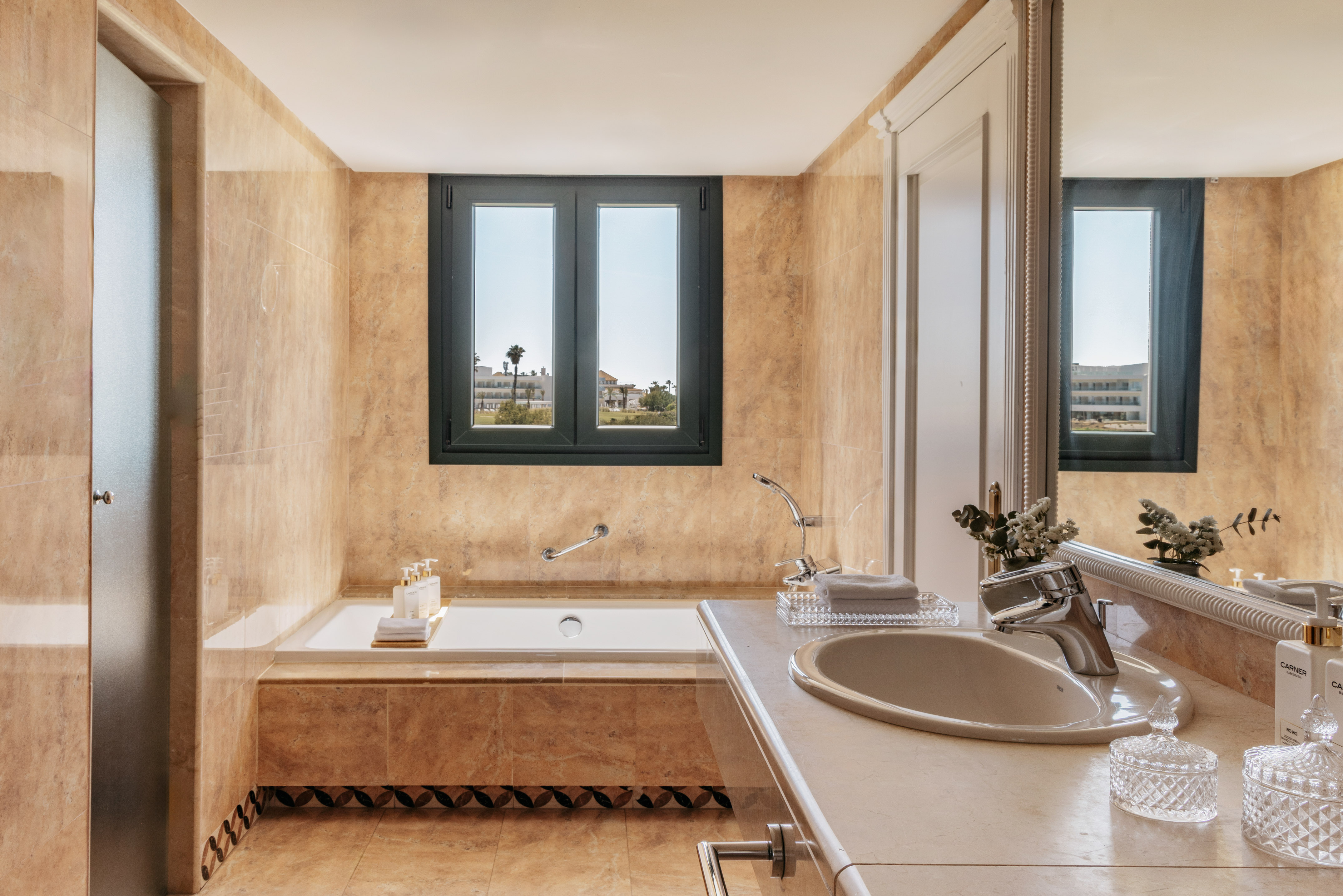 Elegant beige marble bathroom with built-in tub and outdoor window view.