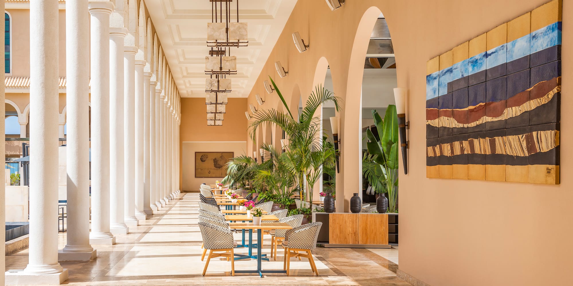 Resort patio with white columns, outdoor tables, tropical plants, and abstract art.