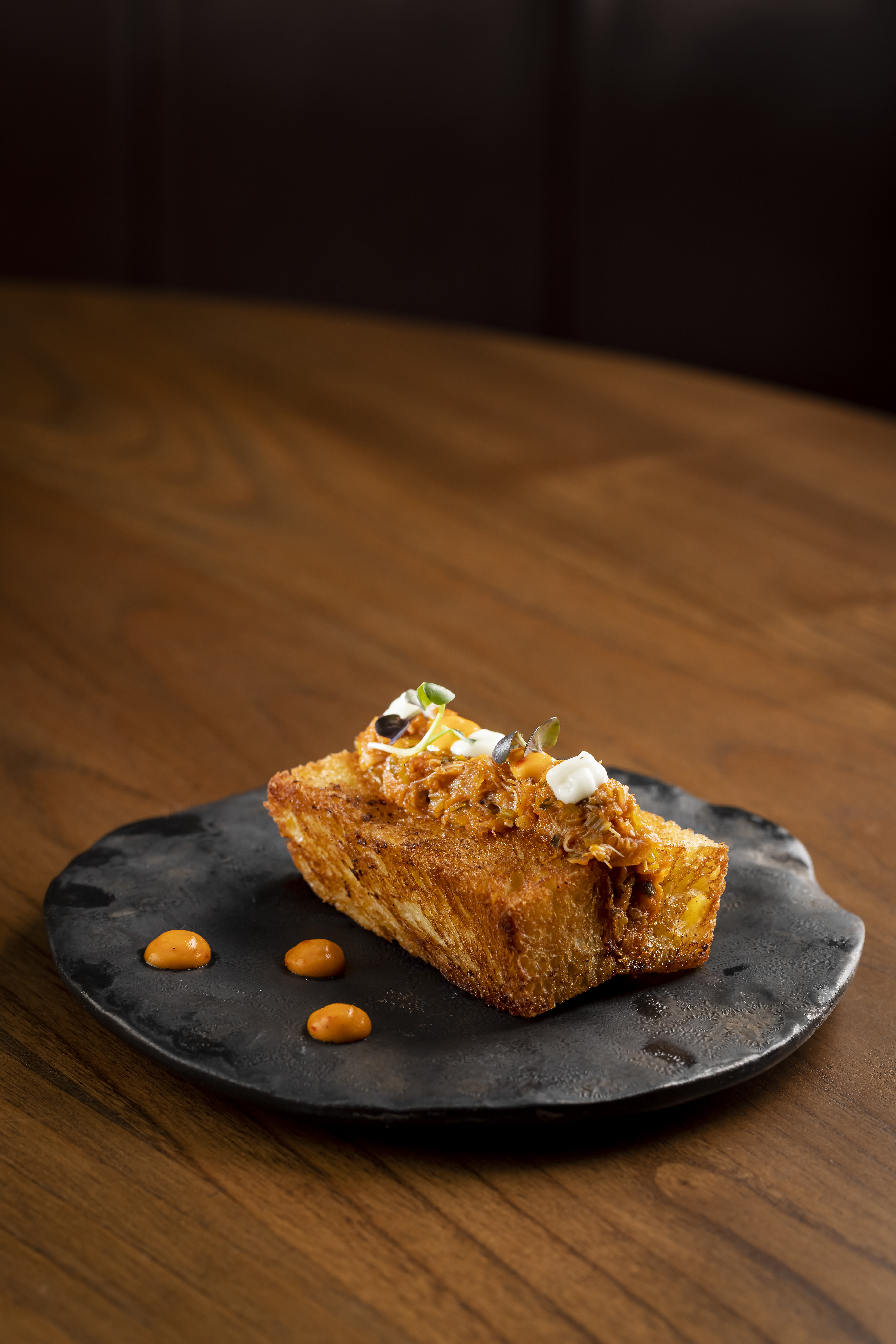 Gourmet crispy toast with savory shredded topping, microgreens, and orange sauce.