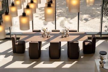 Modern conference table and chairs under pendant lights with large windows.