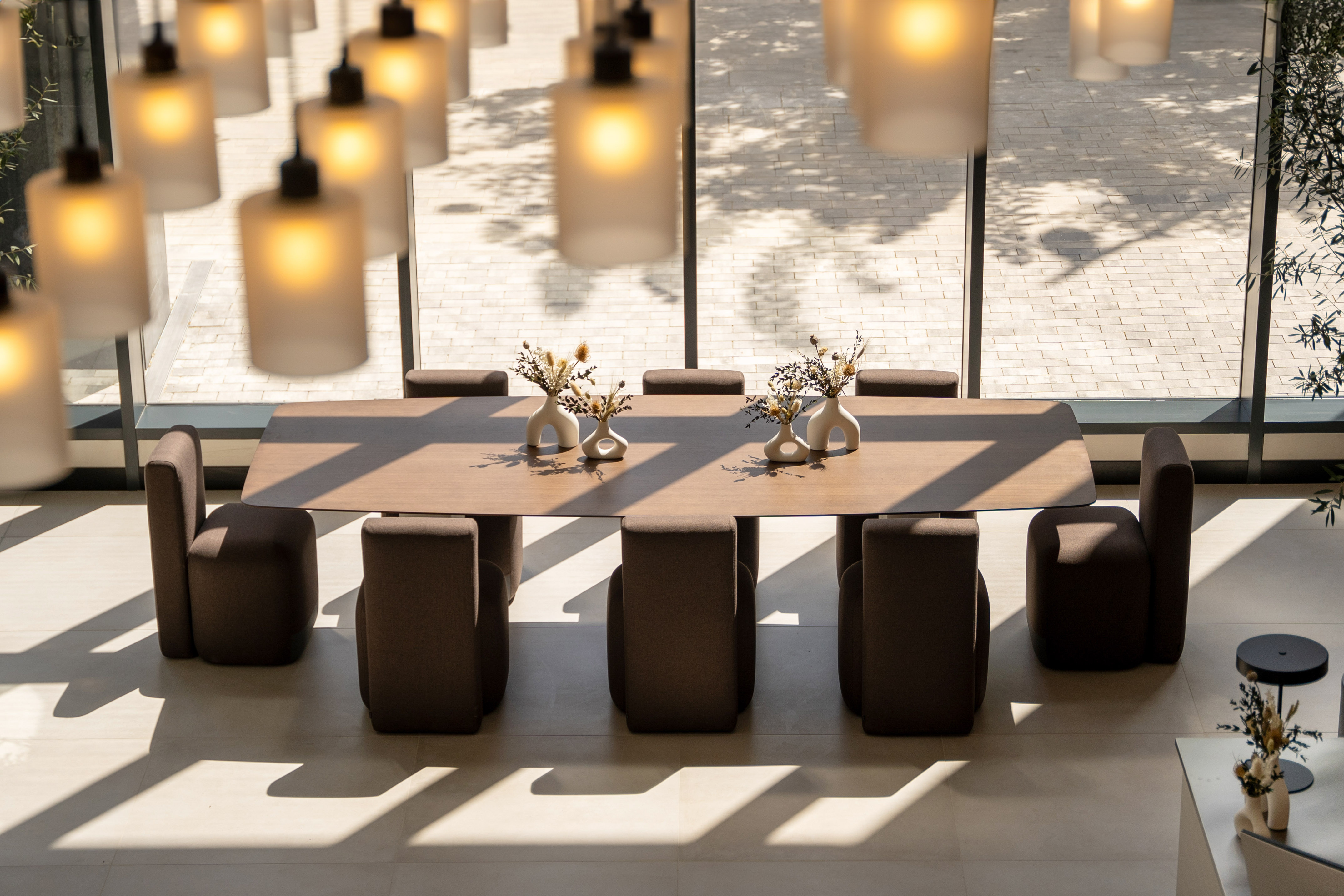 Modern conference table and chairs under pendant lights with large windows.
