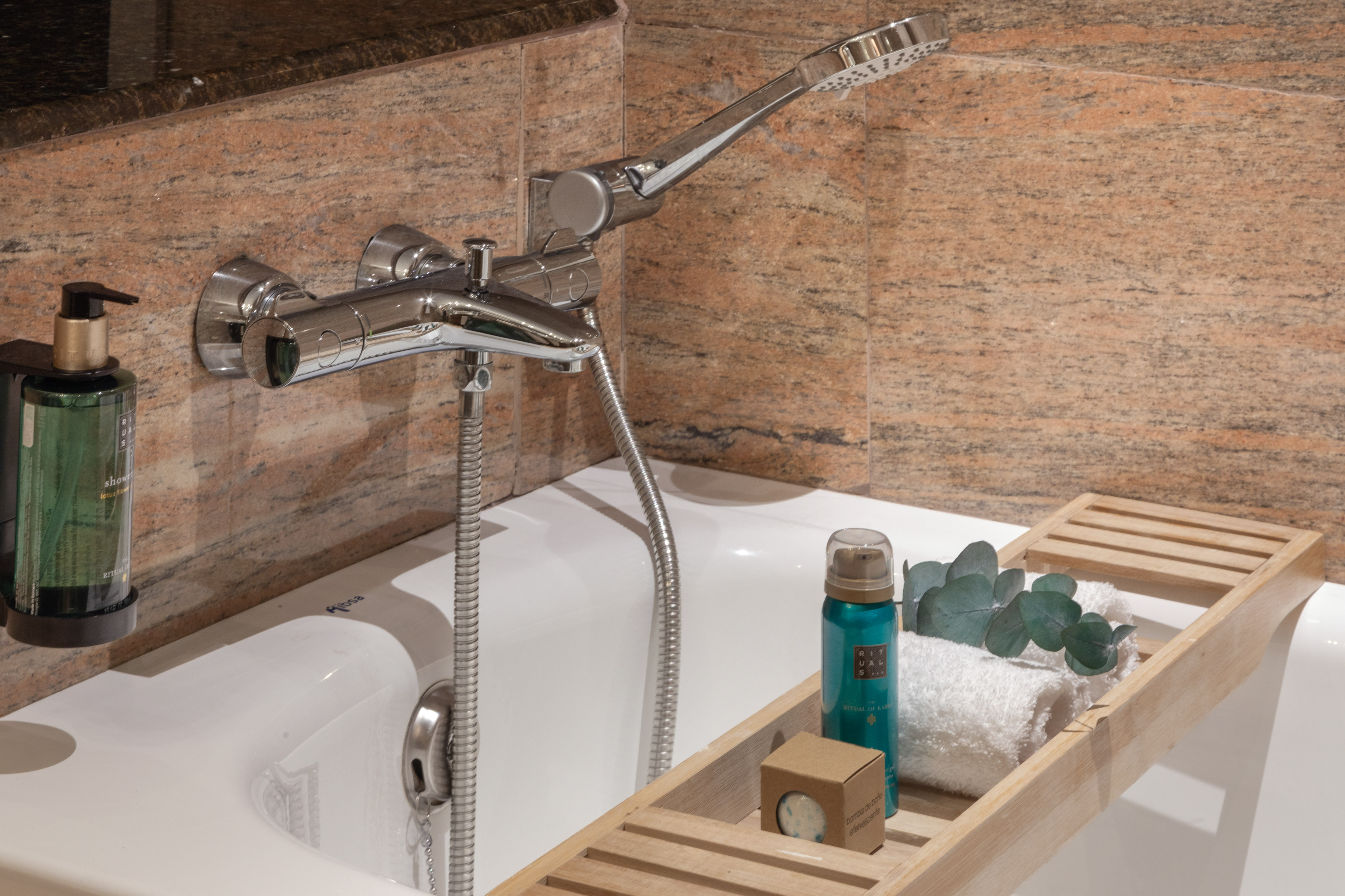 Bañera con grifo de ducha cromado, productos de spa y bandeja de madera.