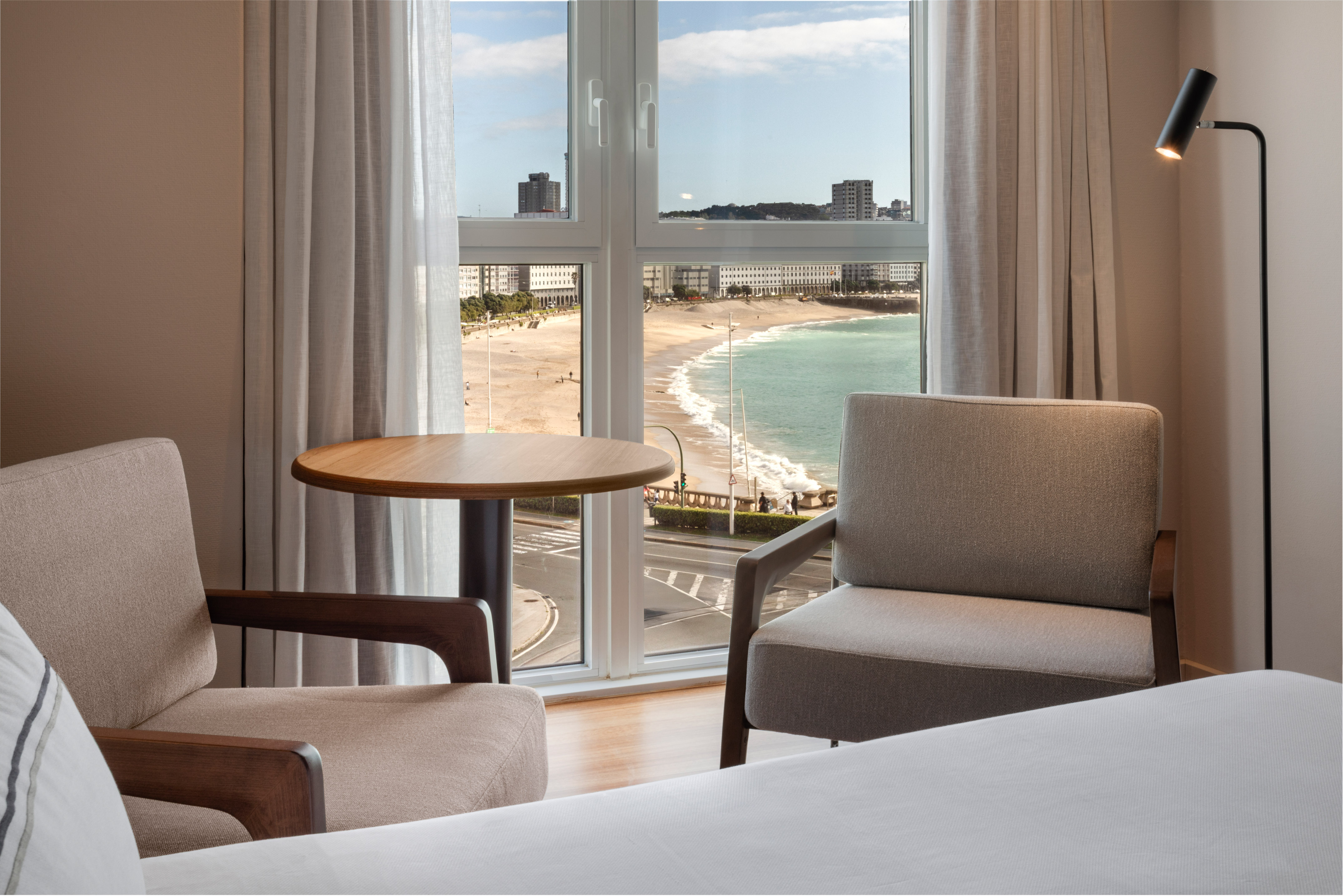 Hotel room with ocean beach view, two armchairs, table by window.