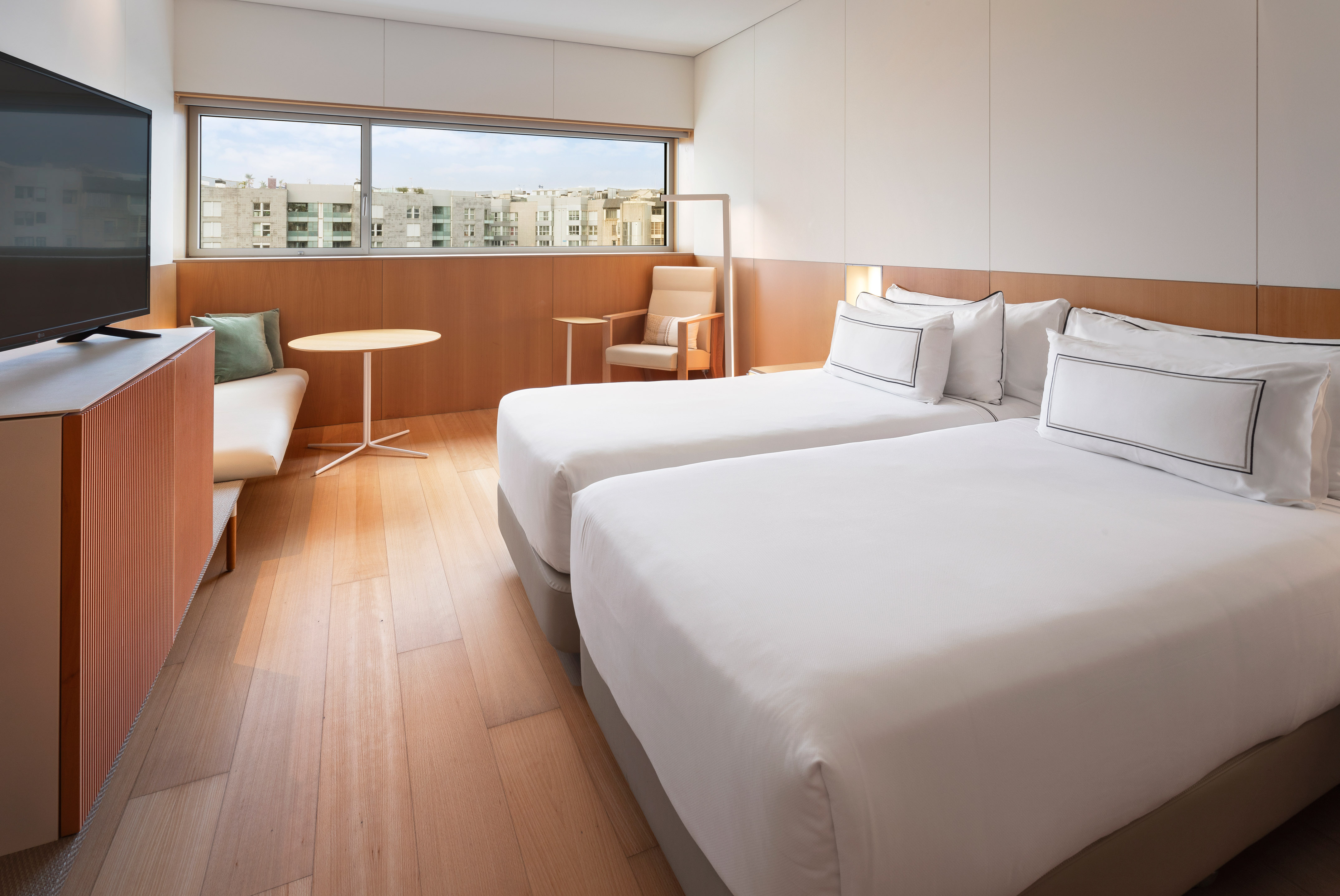 Modern hotel room with two single beds, city view, and wooden floor.