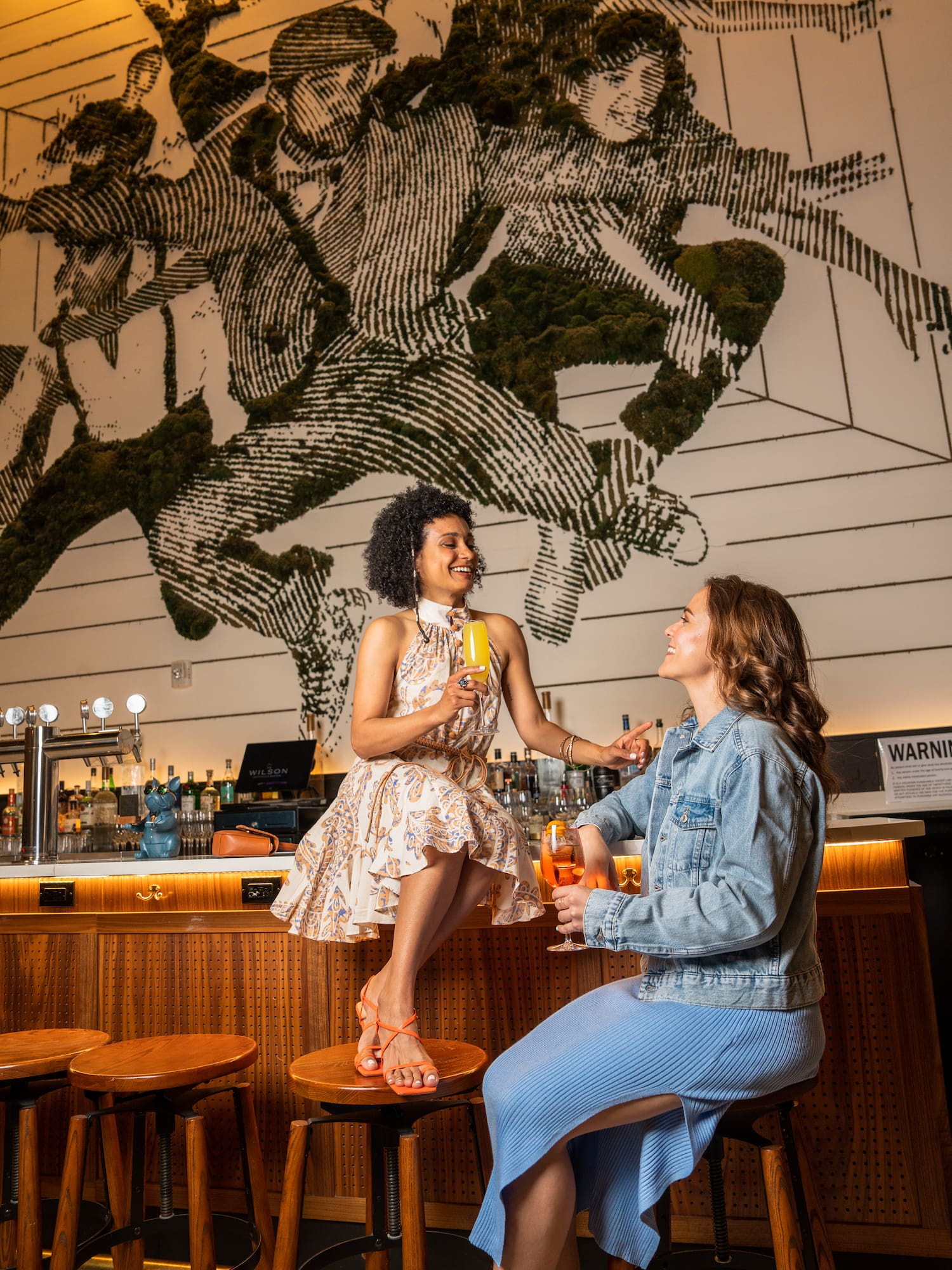two women sitting on stools in a bar