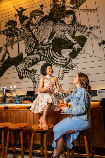 two women sitting on stools in a bar