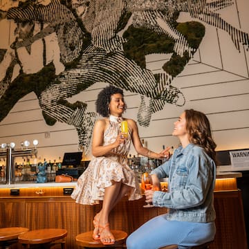 two women sitting on stools in a bar