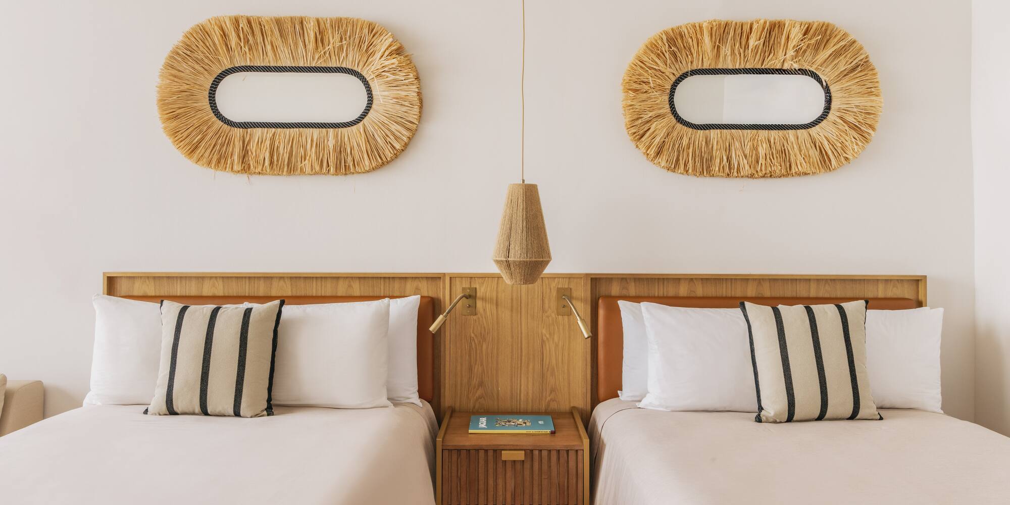 Hotel twin room with wooden headboards, neutral bedding, and straw mirrors.