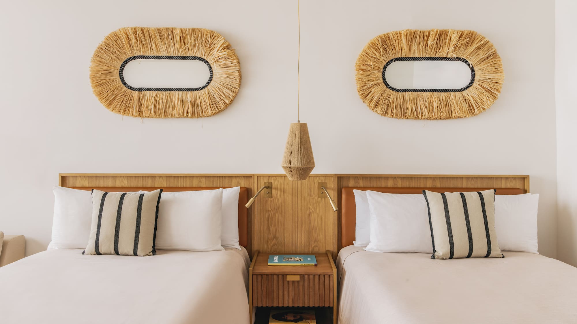 Hotel twin room with wooden headboards, neutral bedding, and straw mirrors.