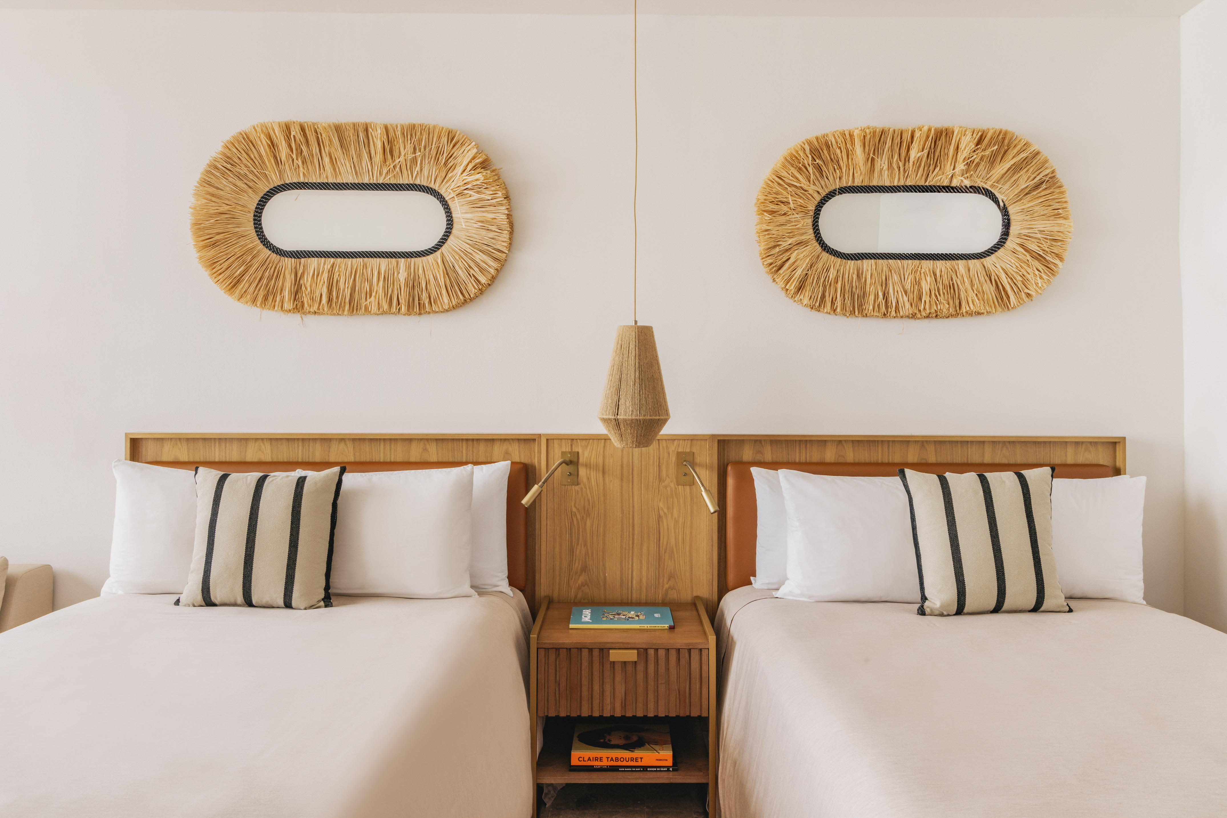 Hotel twin room with wooden headboards, neutral bedding, and straw mirrors.