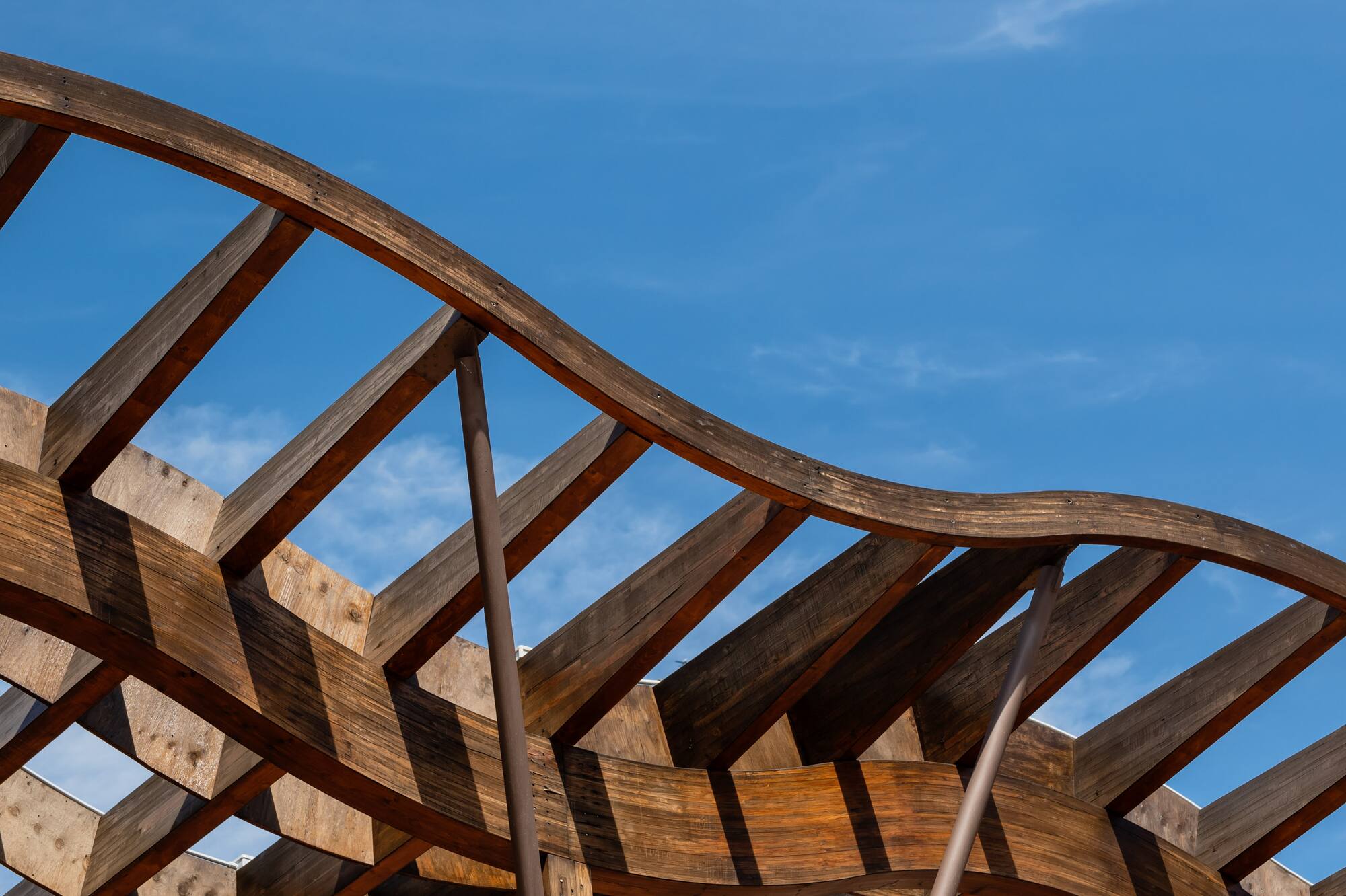 Geometric wooden pergola design under clear blue sky.