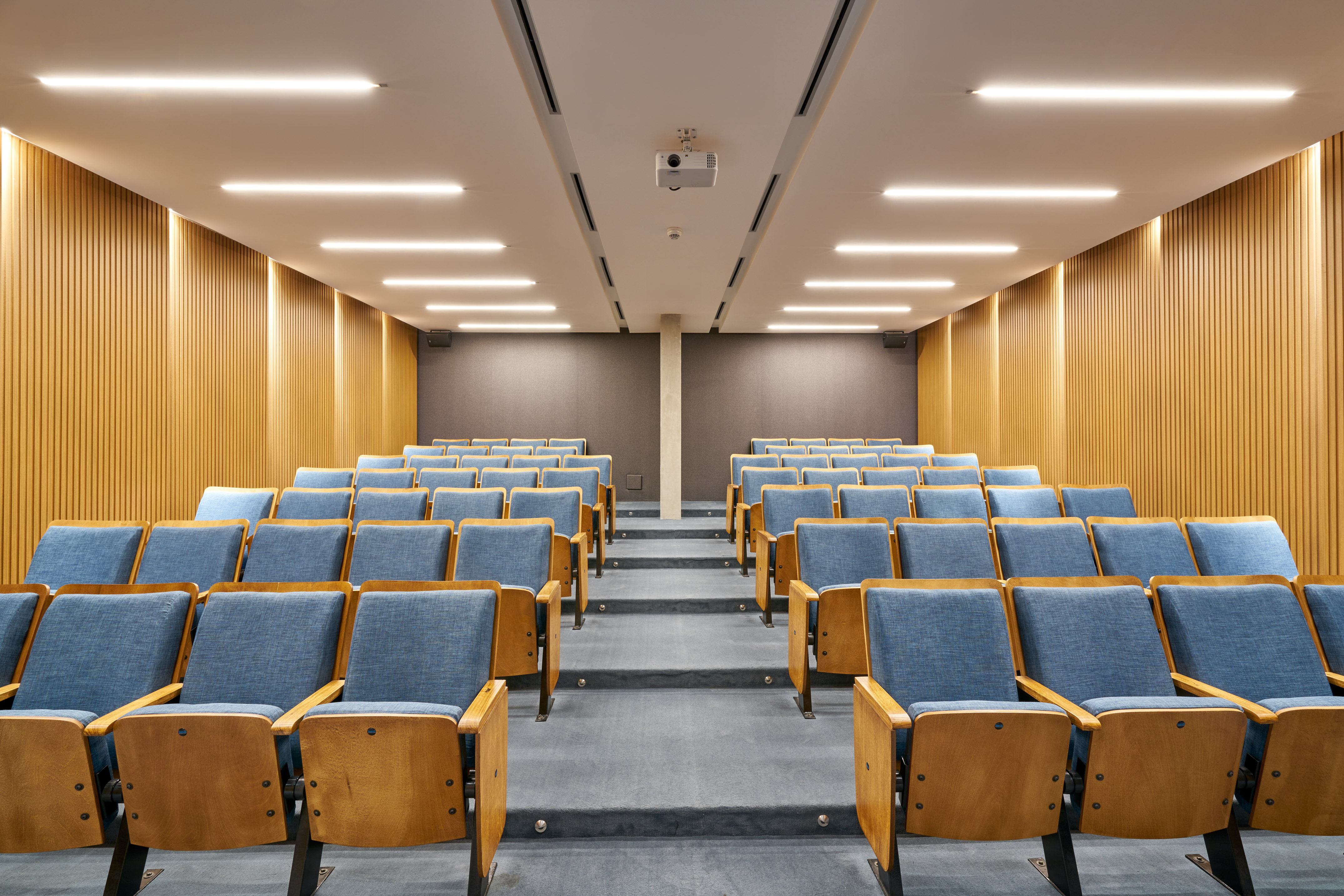 Modern lecture hall with blue chairs, wood paneling, and projector.