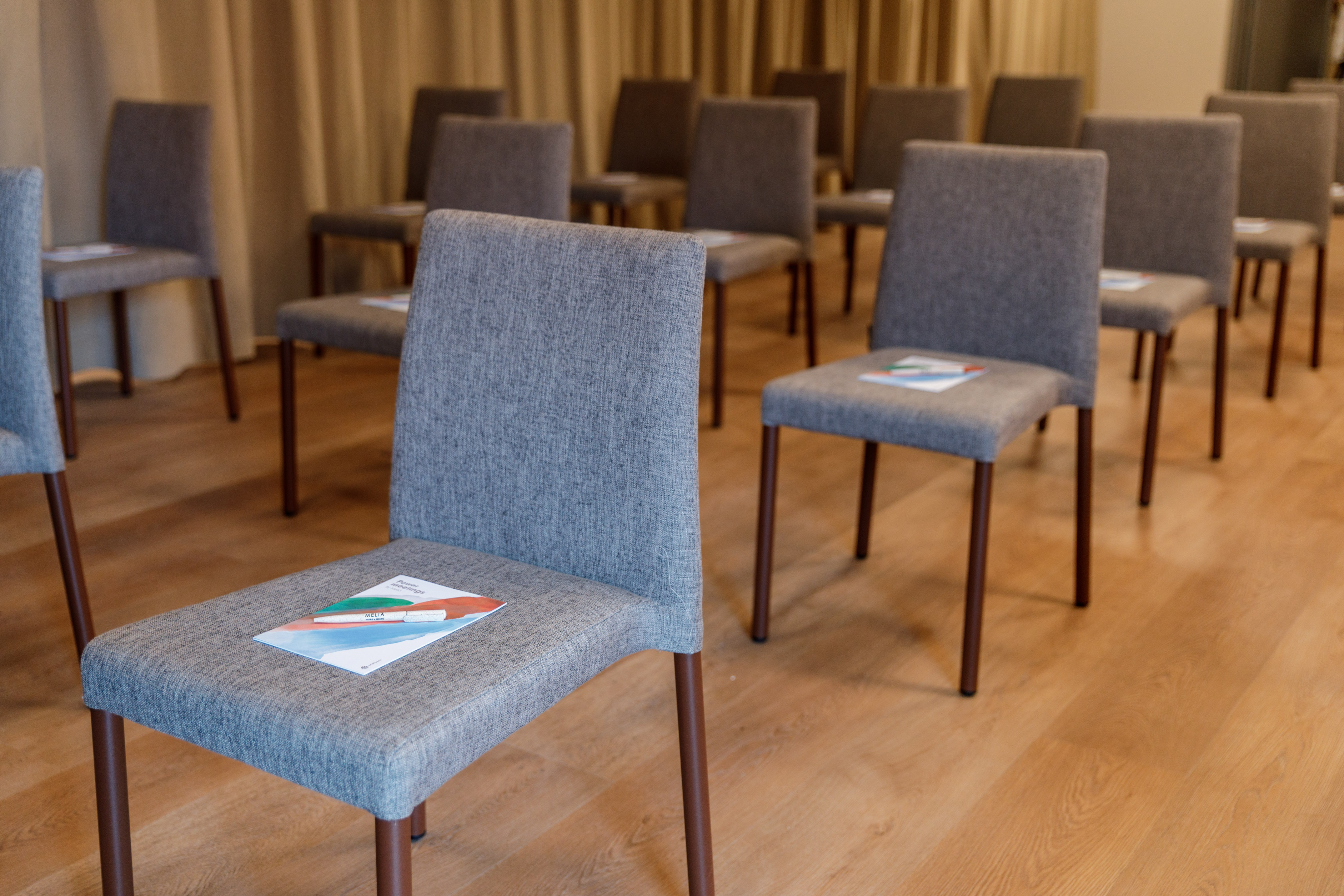 Meeting room with rows of gray chairs, brochure and pen on front seat.
