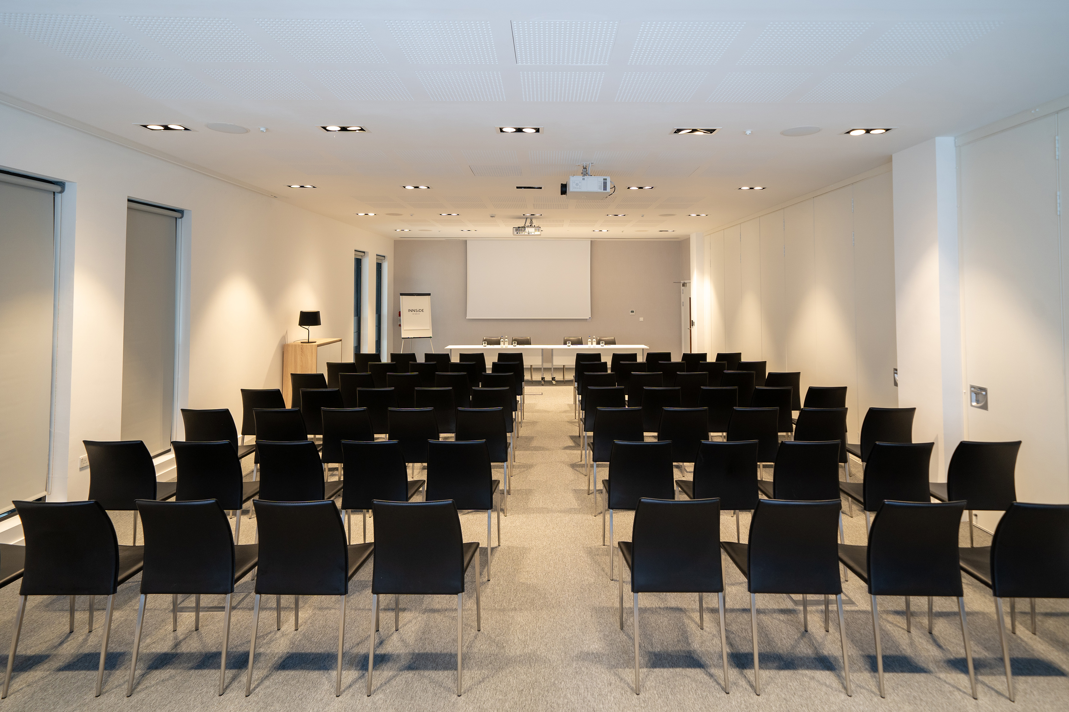 Empty modern conference room with black chairs, projector, and screen.
