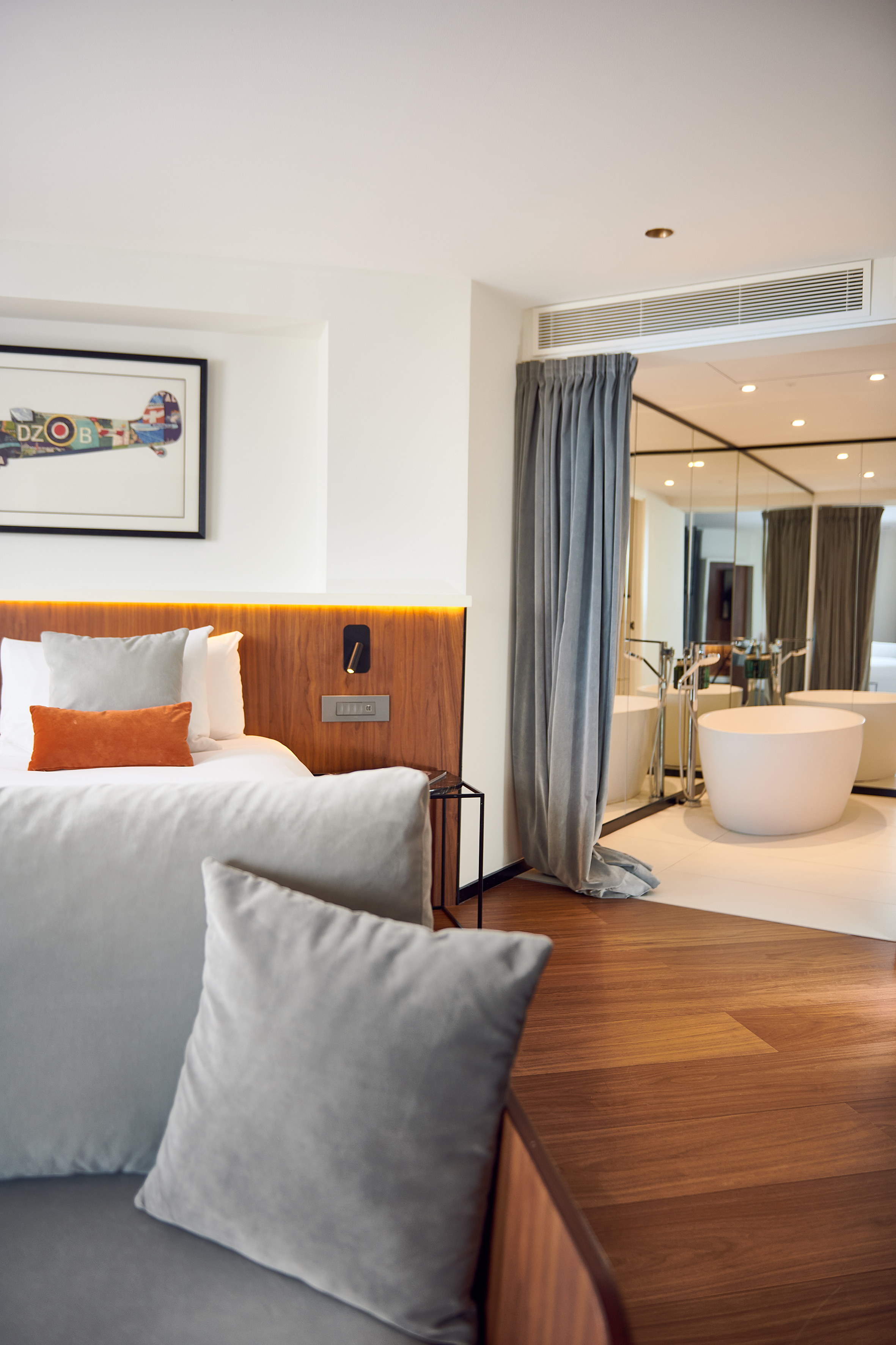 Modern hotel room with bed and open plan bathroom featuring freestanding tub.