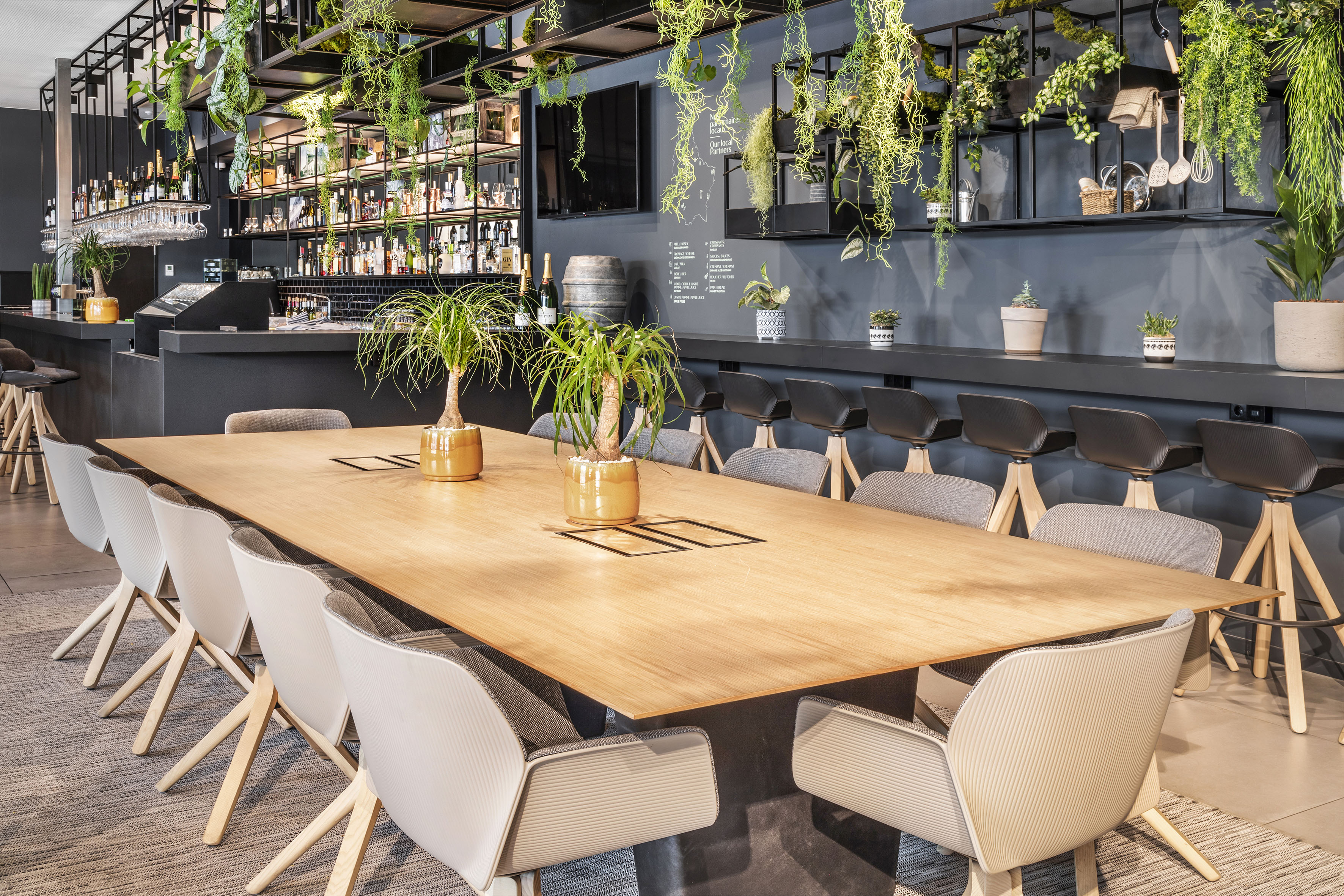 Sleek bar and meeting room with wooden table, modern seating, and lush plants. - De Gaart, Cuisine locale - INNSiDE Luxembourg, Luxembourg