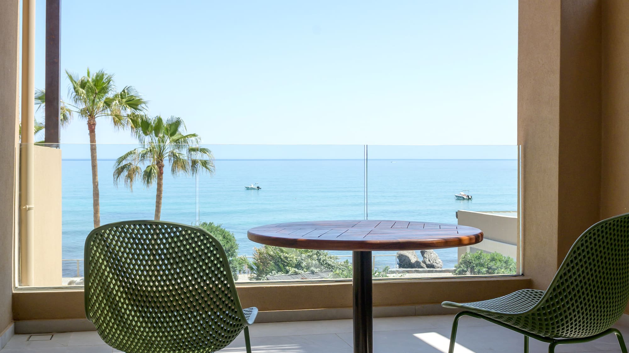 Balcony with green chairs, wooden table, ocean view, and palm trees.