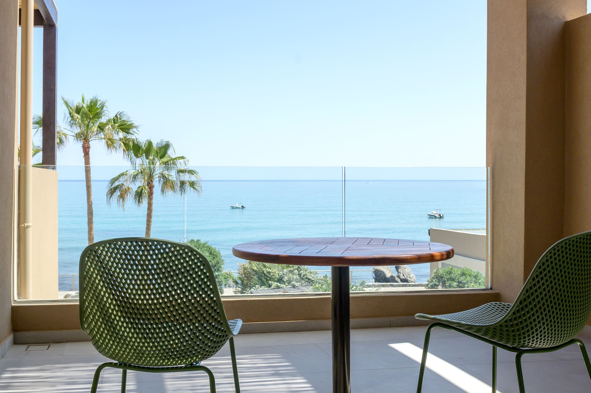 Balcony with green chairs, wooden table, ocean view, and palm trees.