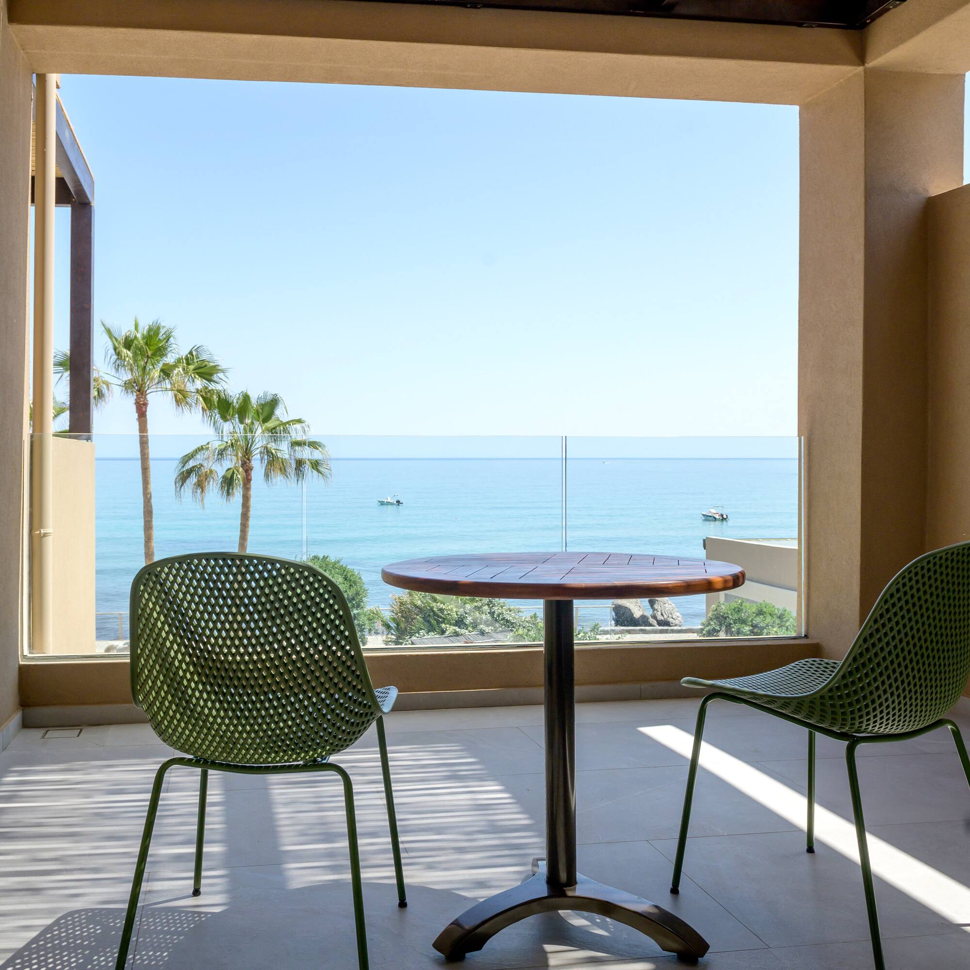 Balcony with green chairs, wooden table, ocean view, and palm trees.