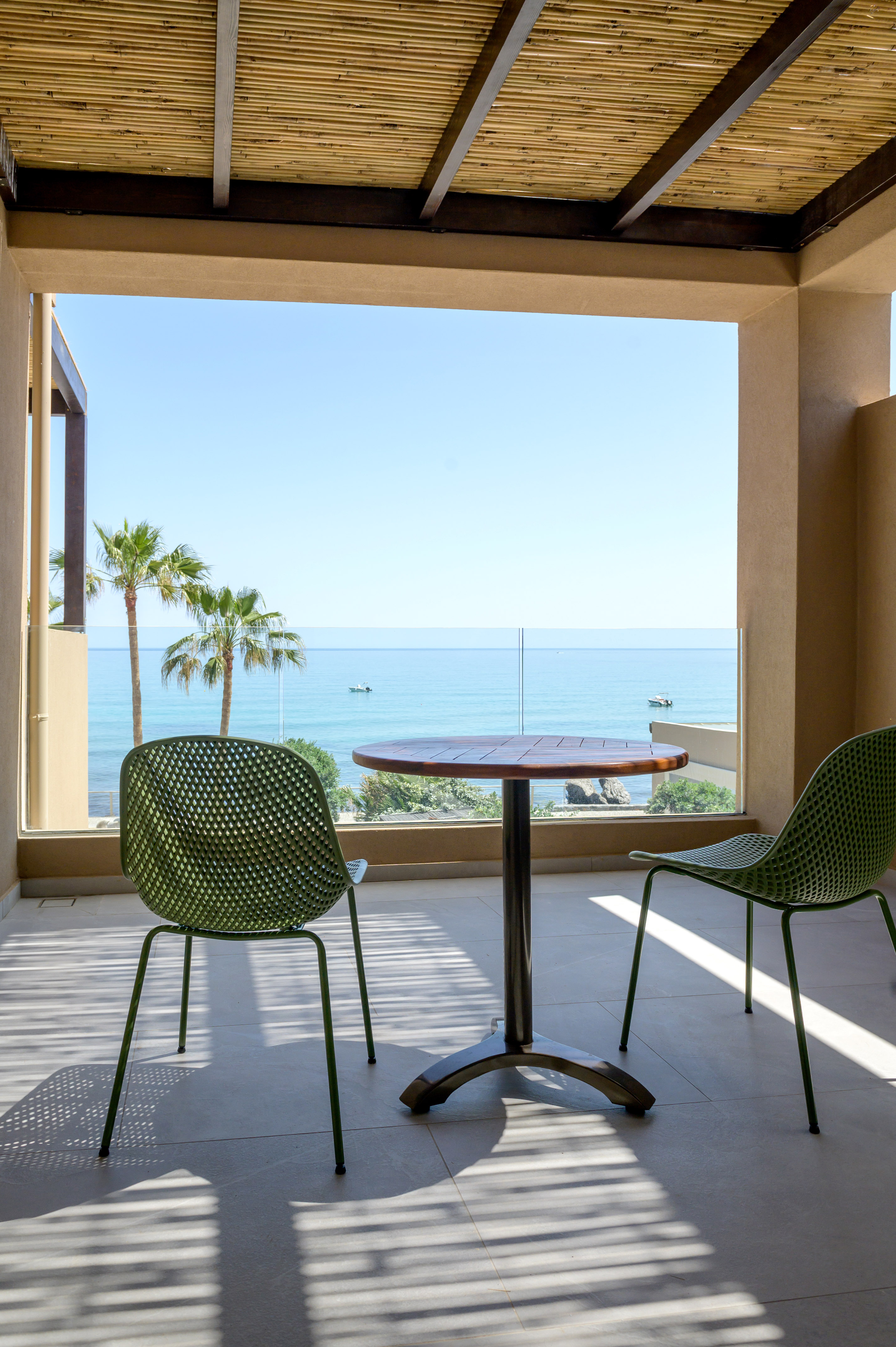 Balcony with green chairs, wooden table, ocean view, and palm trees.