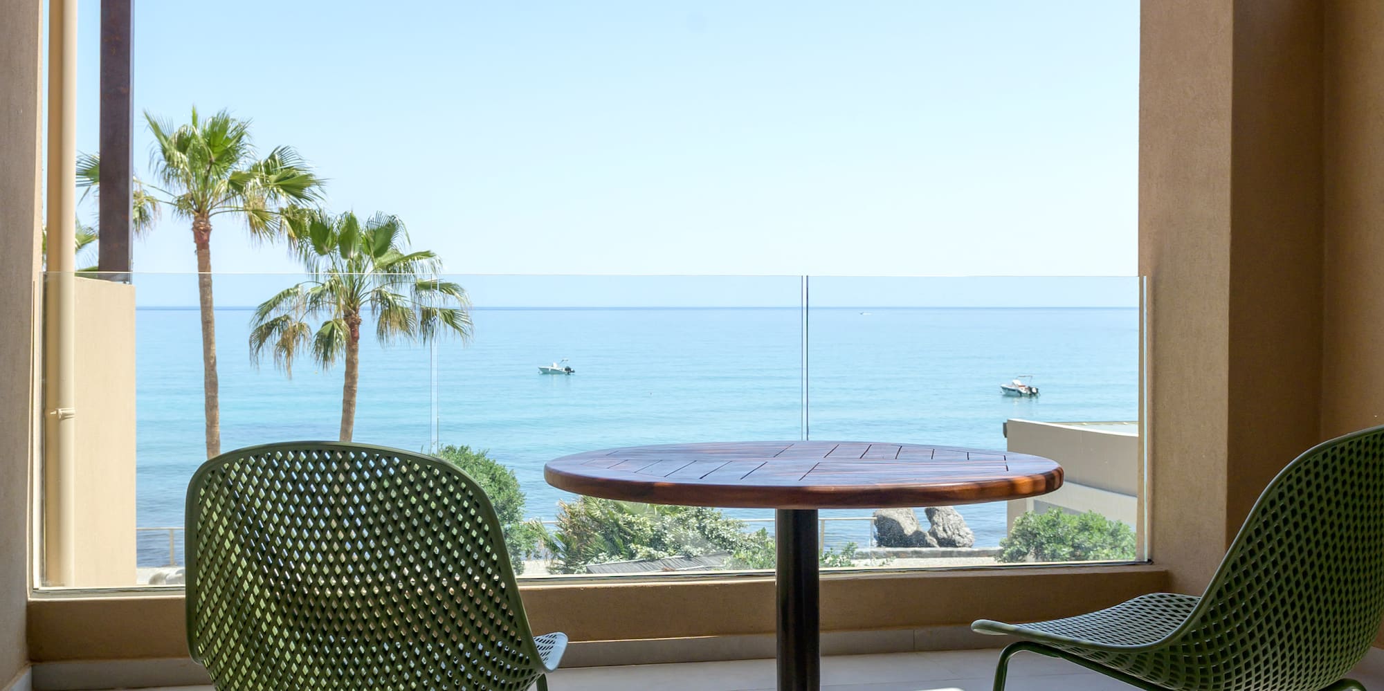 Balcony with green chairs, wooden table, ocean view, and palm trees.