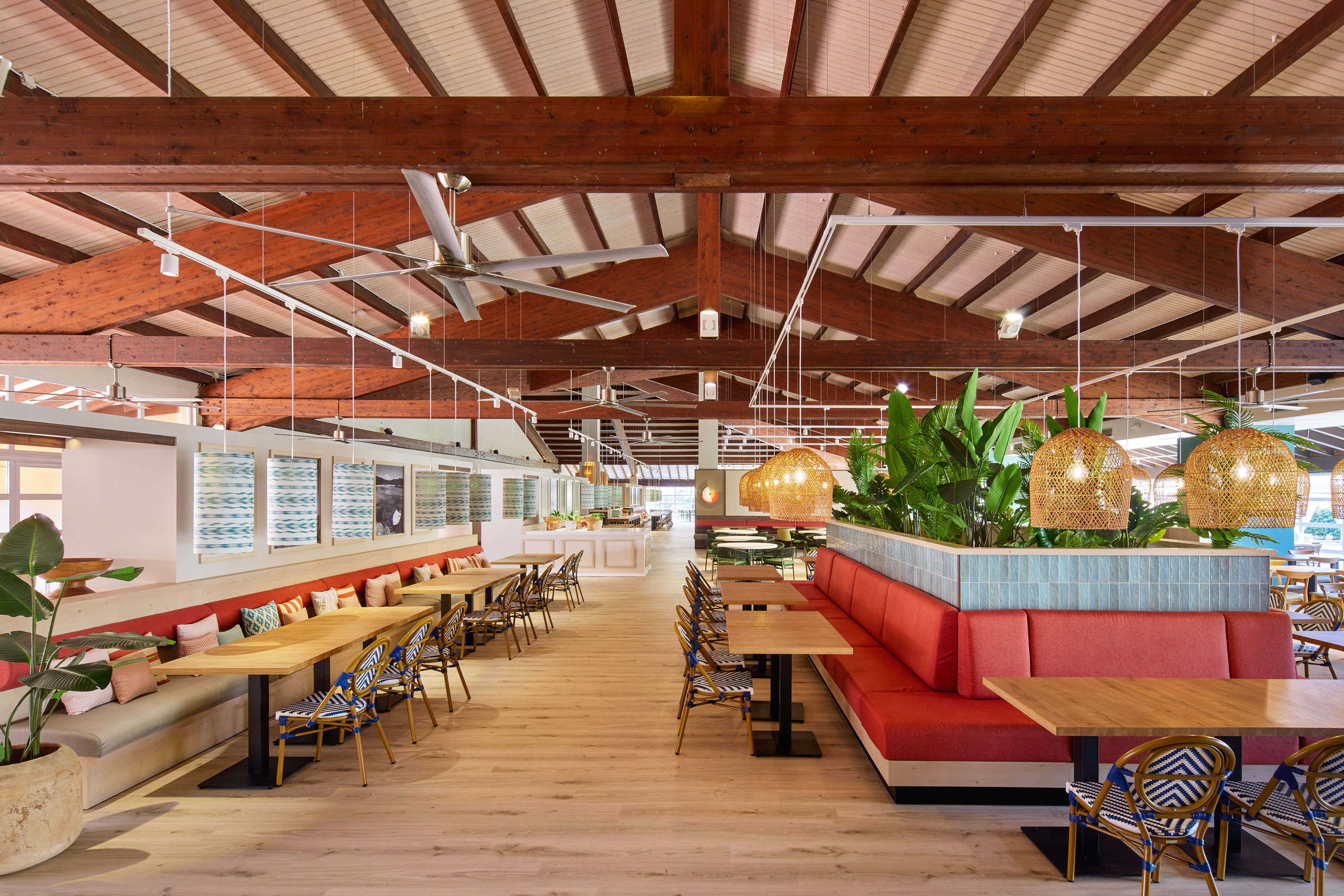 Modern tropical restaurant interior with red booths, wooden tables, and plants.