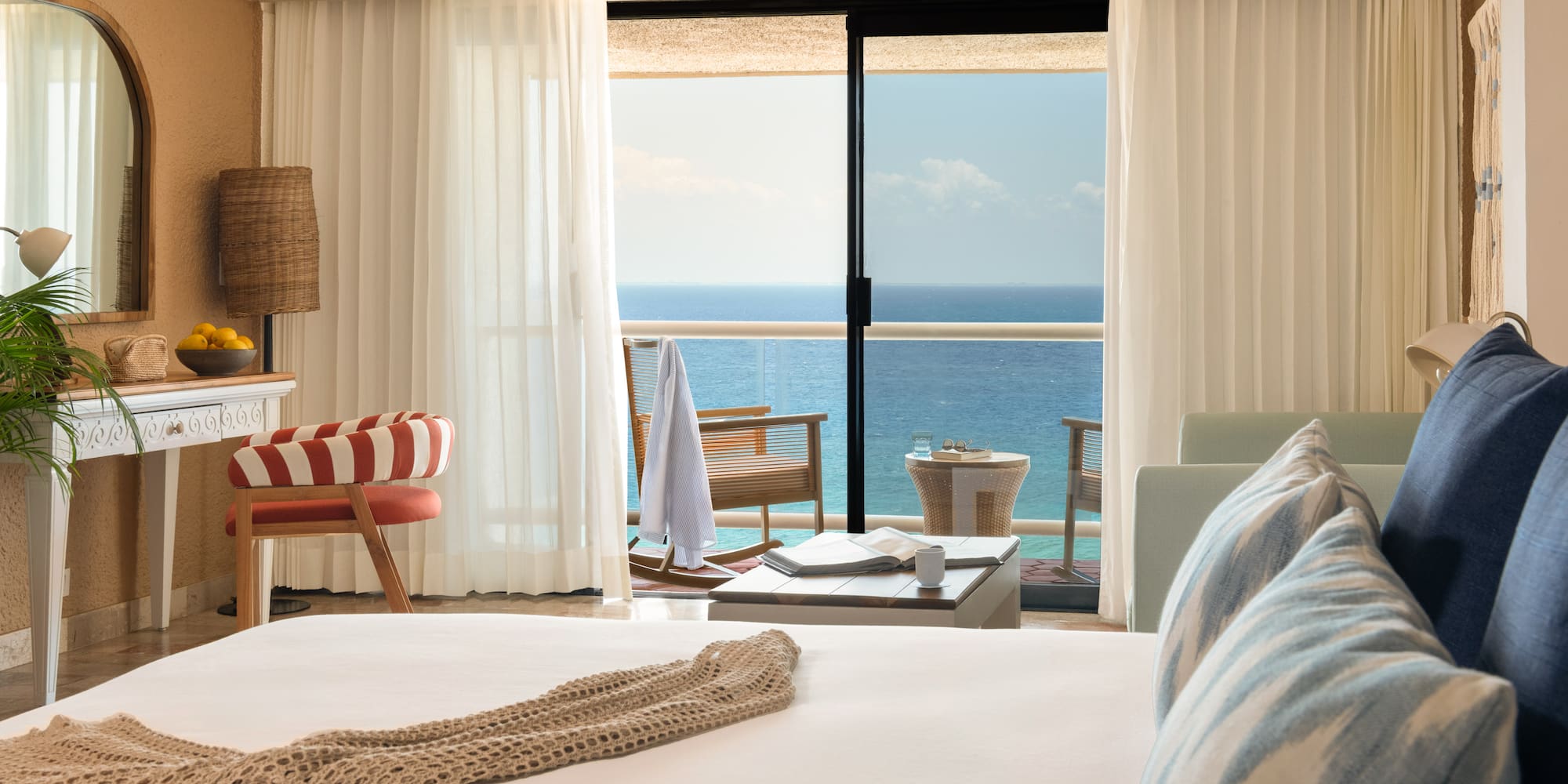 Hotel room with ocean view balcony, white bed, and tropical decor.