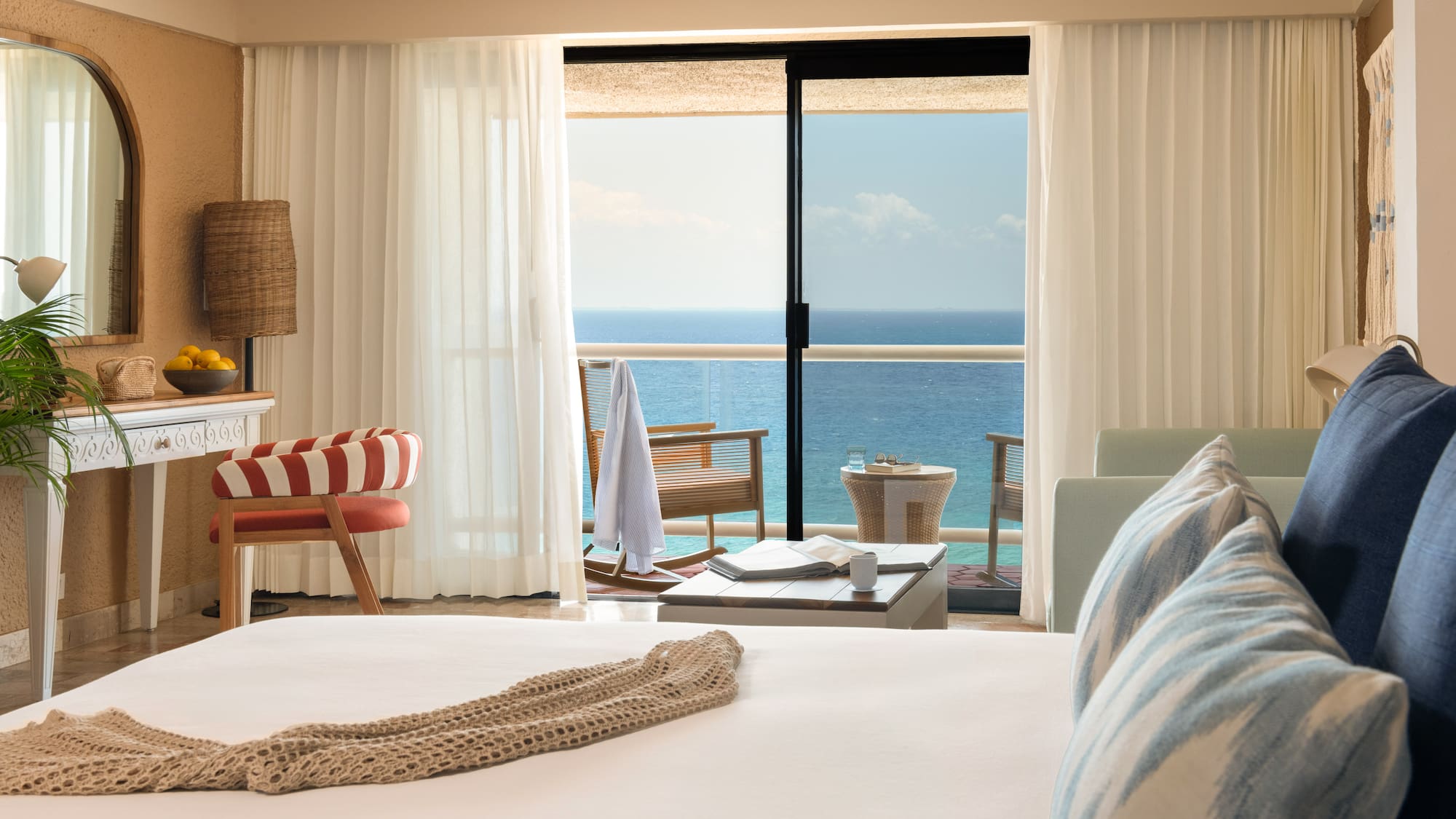 Hotel room with ocean view balcony, white bed, and tropical decor.