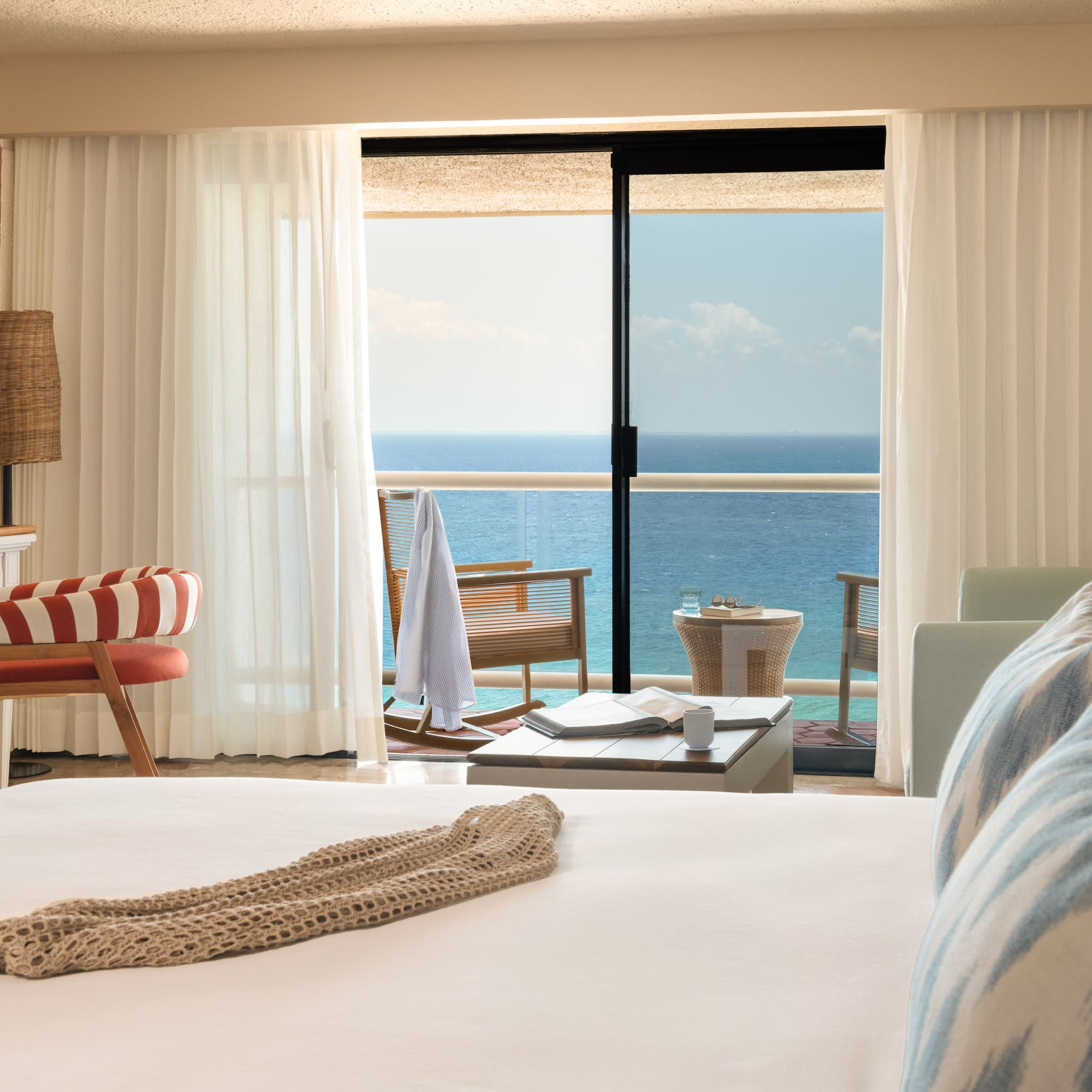 Hotel room with ocean view balcony, white bed, and tropical decor.