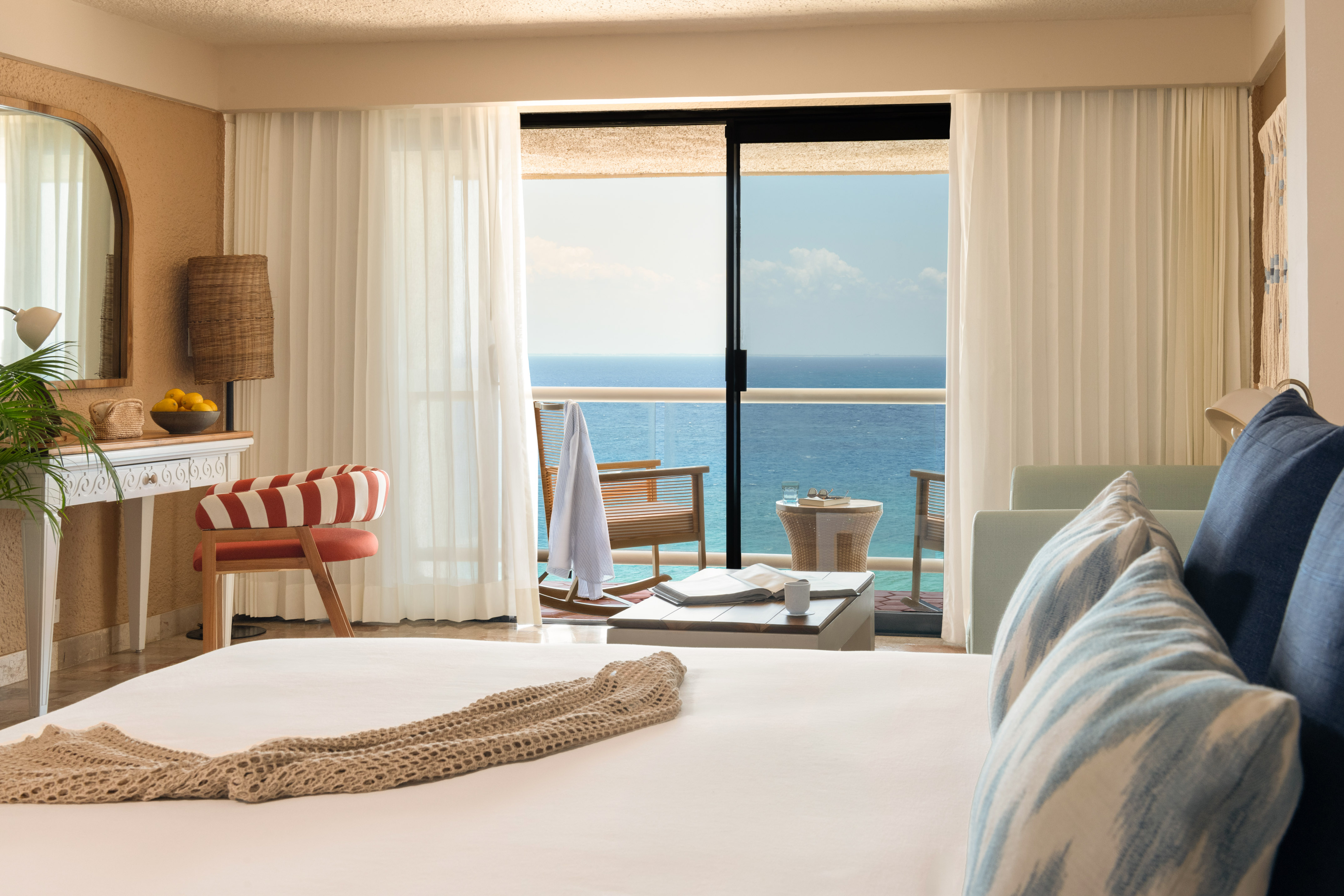 Hotel room with ocean view balcony, white bed, and tropical decor.