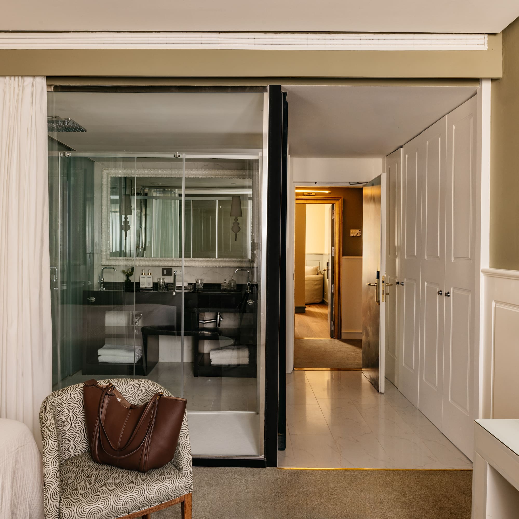 Suite de hotel elegante con baño de cristal, dormitorio y recibidor.