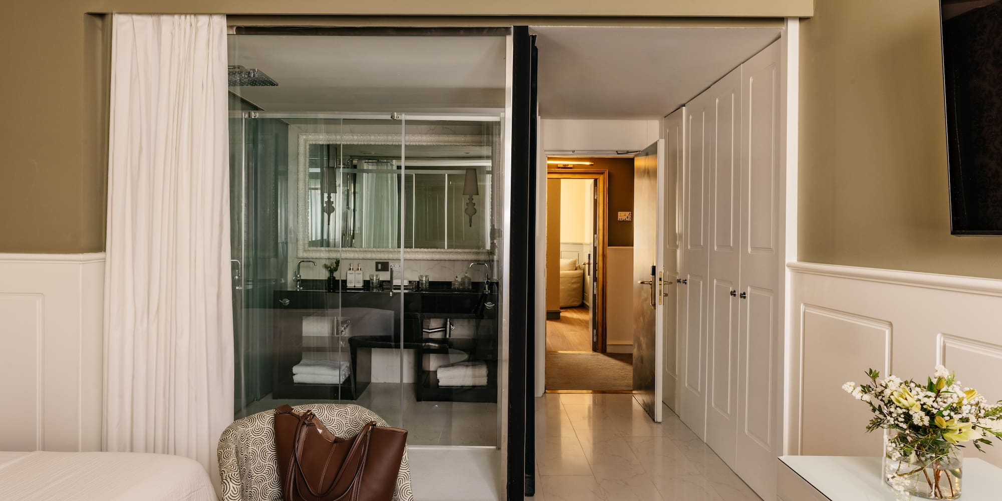 Suite de hotel elegante con baño de cristal, dormitorio y recibidor.