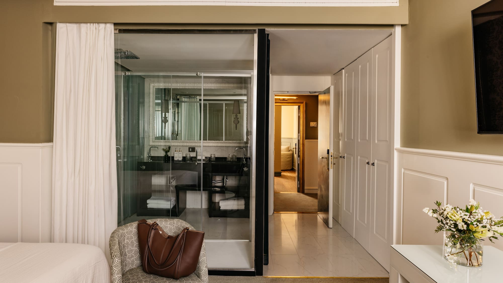 Suite de hotel elegante con baño de cristal, dormitorio y recibidor.