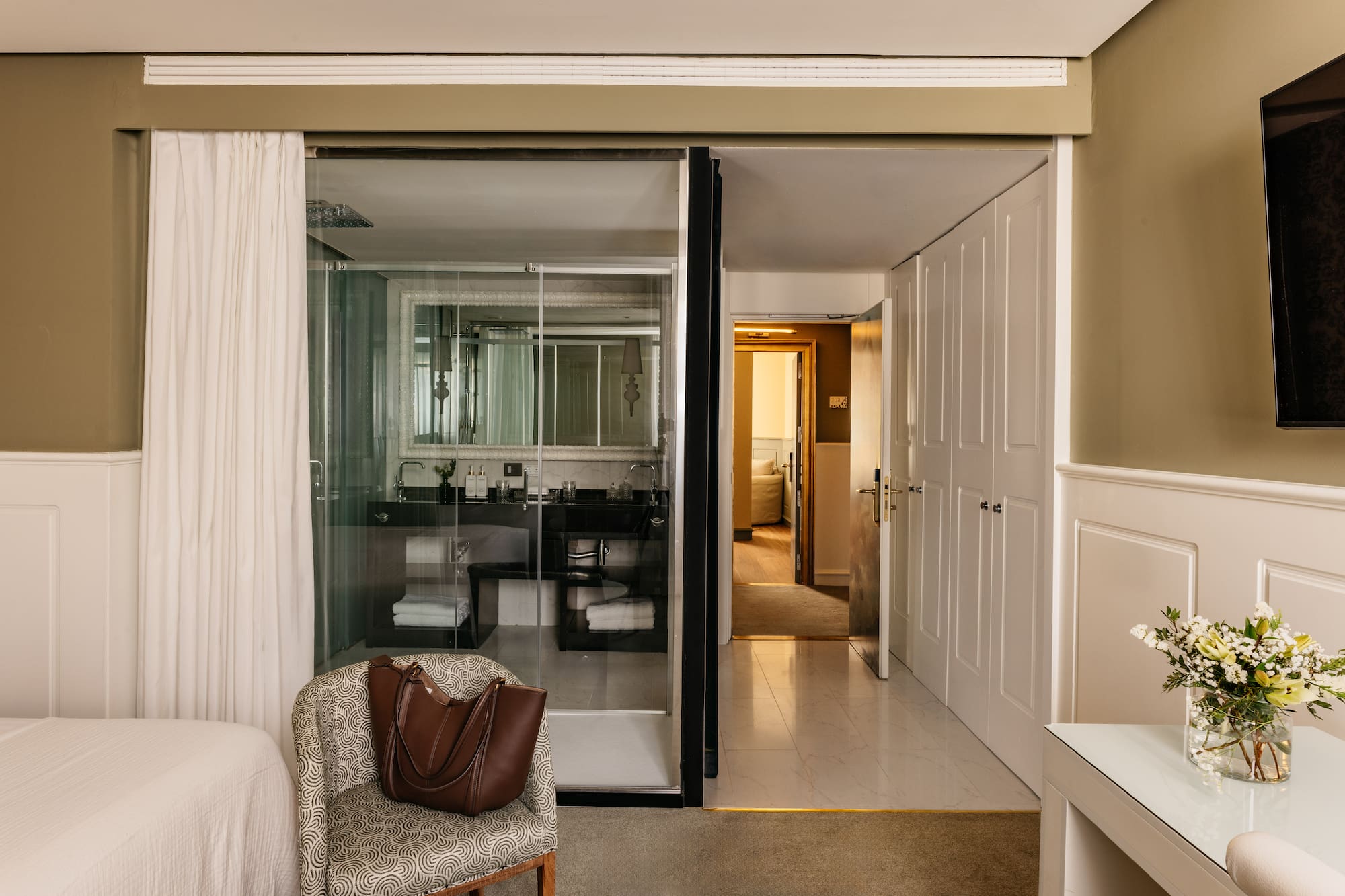 Suite de hotel elegante con baño de cristal, dormitorio y recibidor.