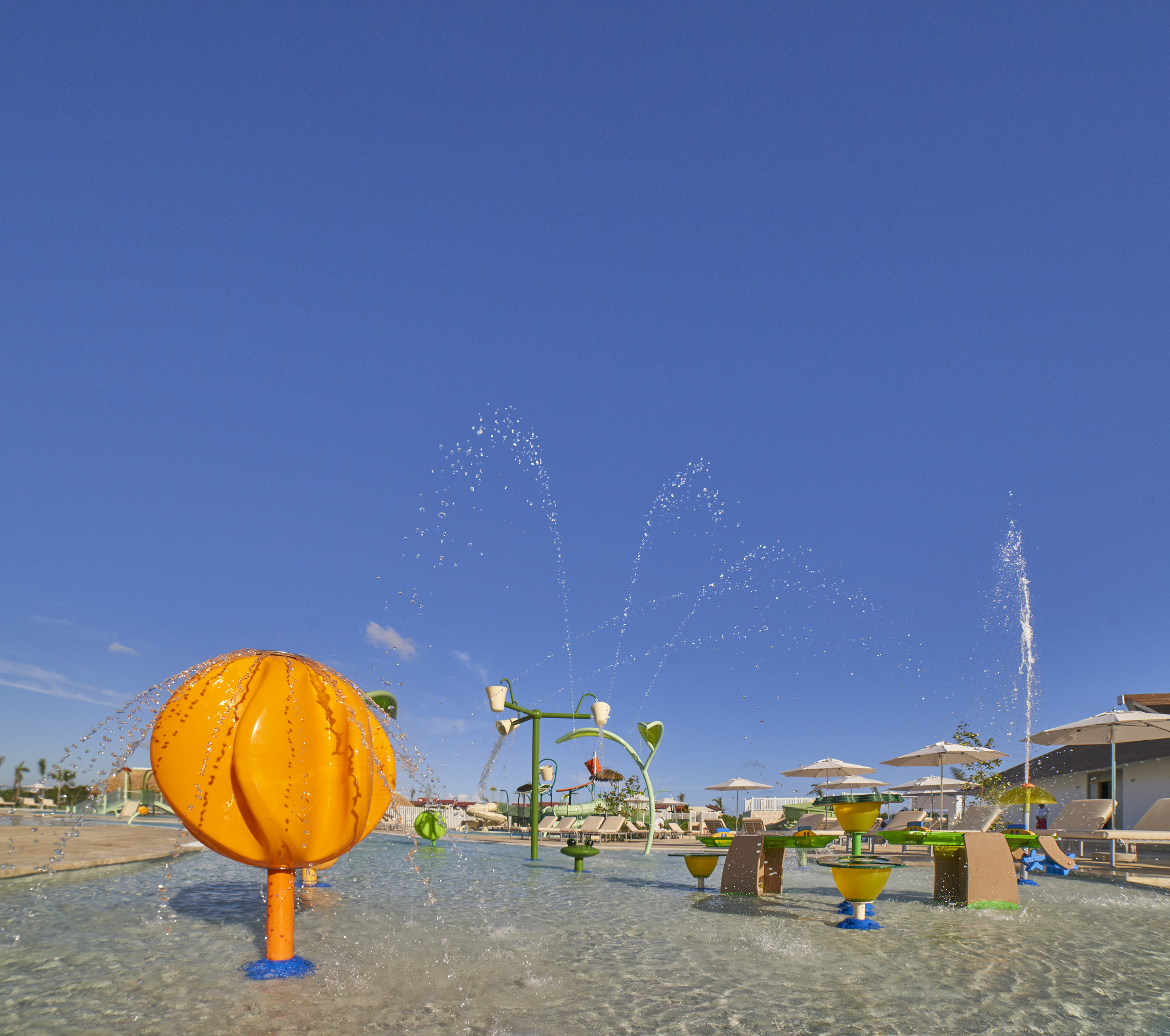 Kids' splash pad with colorful water features at a sunny resort.