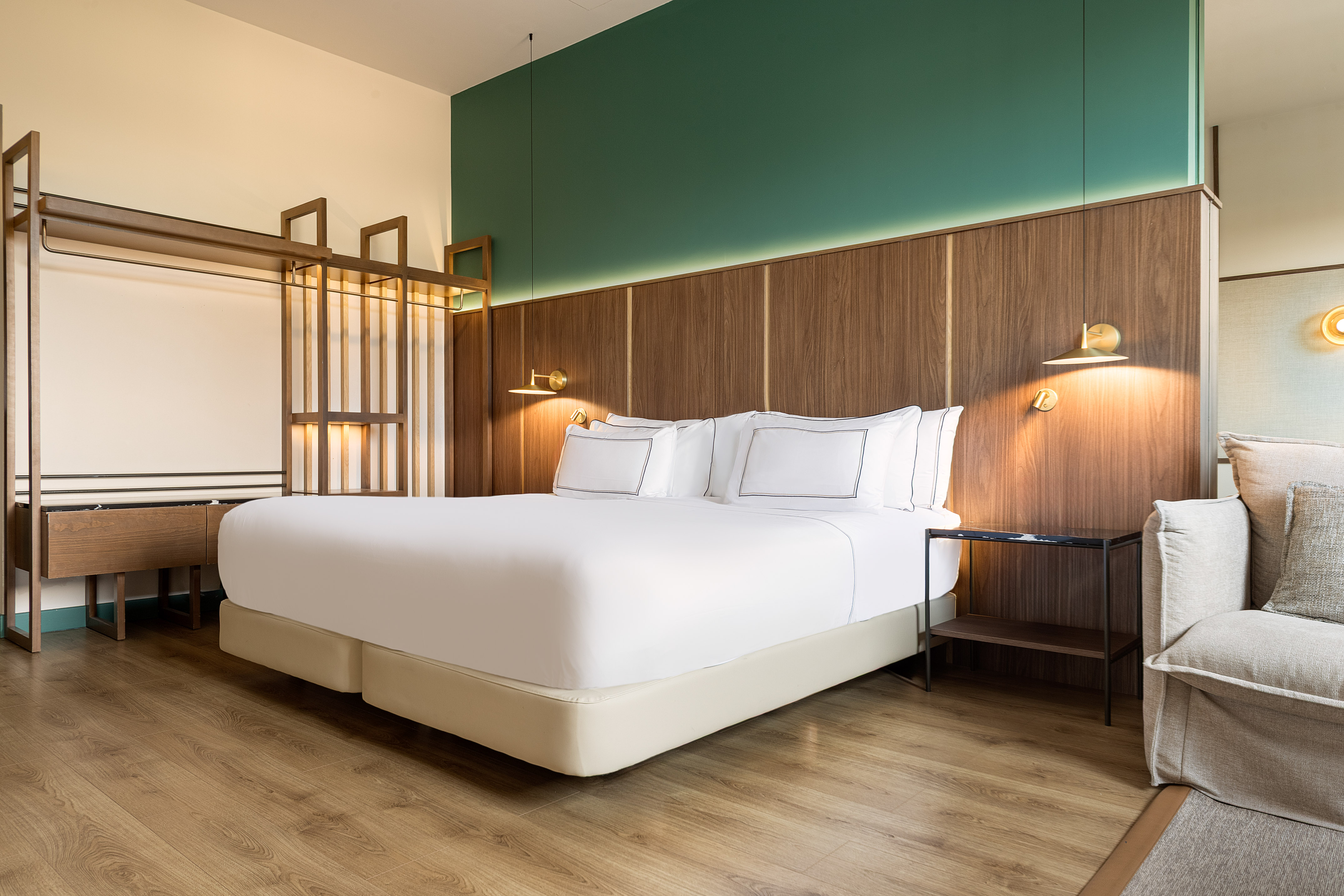 Modern hotel bedroom with white bed, wood headboard, and green wall.