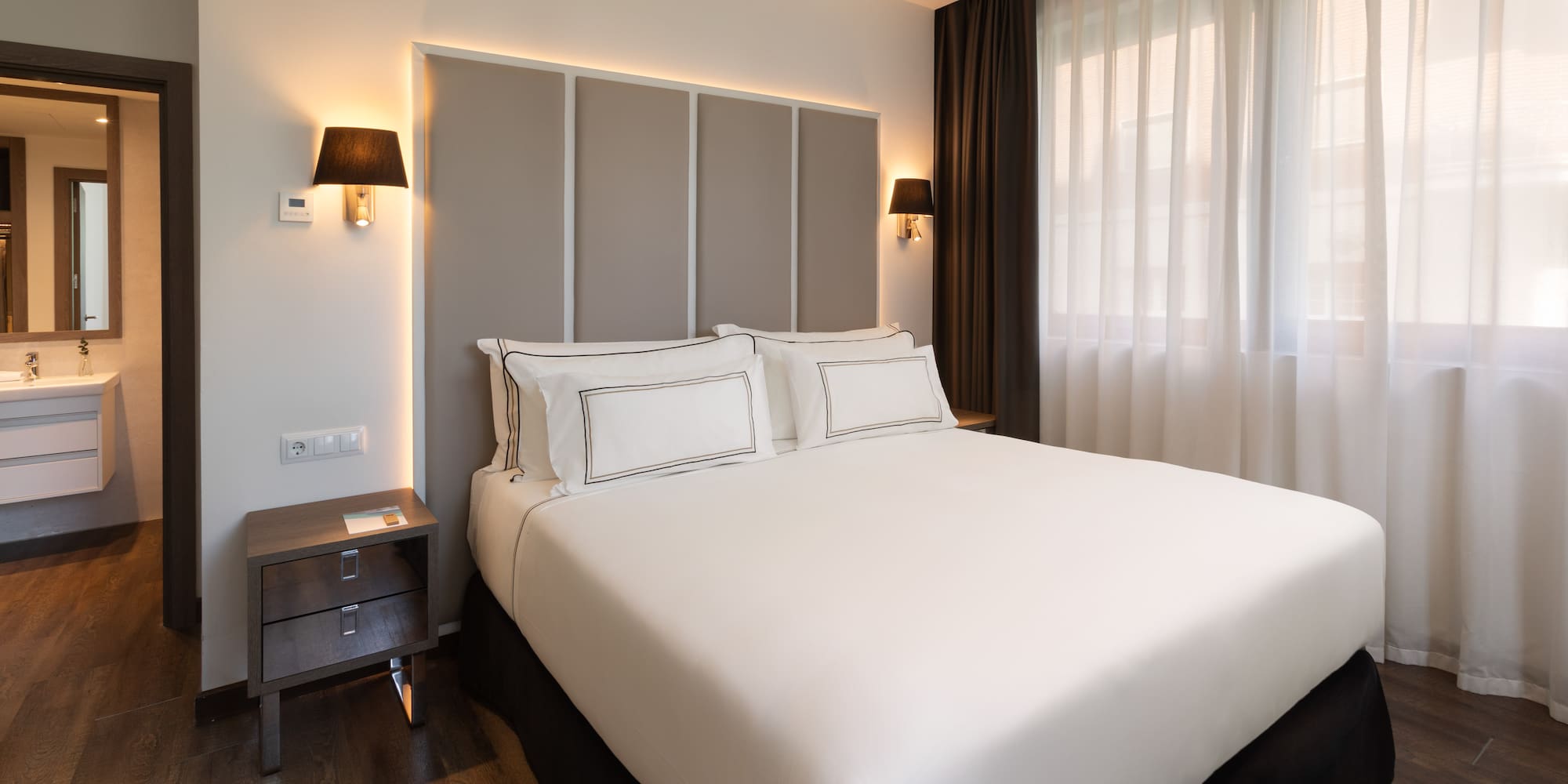 Habitación de hotel moderna con cama doble, cabecero iluminado y baño.